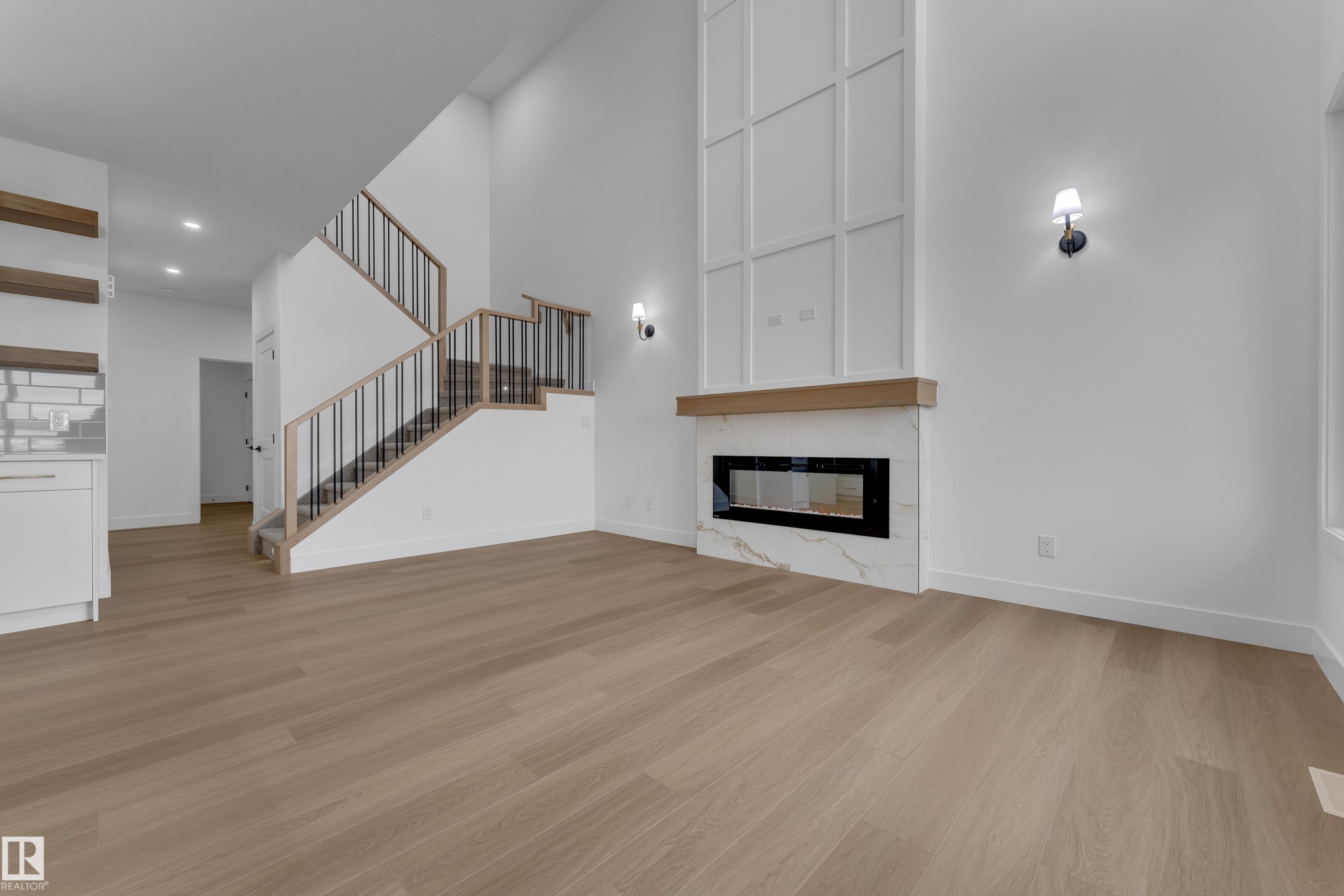 High ceilings, wood-finish flooring, a contemporary linear fireplace with a stone surround, and an open-tread staircase with metal balusters - 794 Bank Drive, Leduc, AB