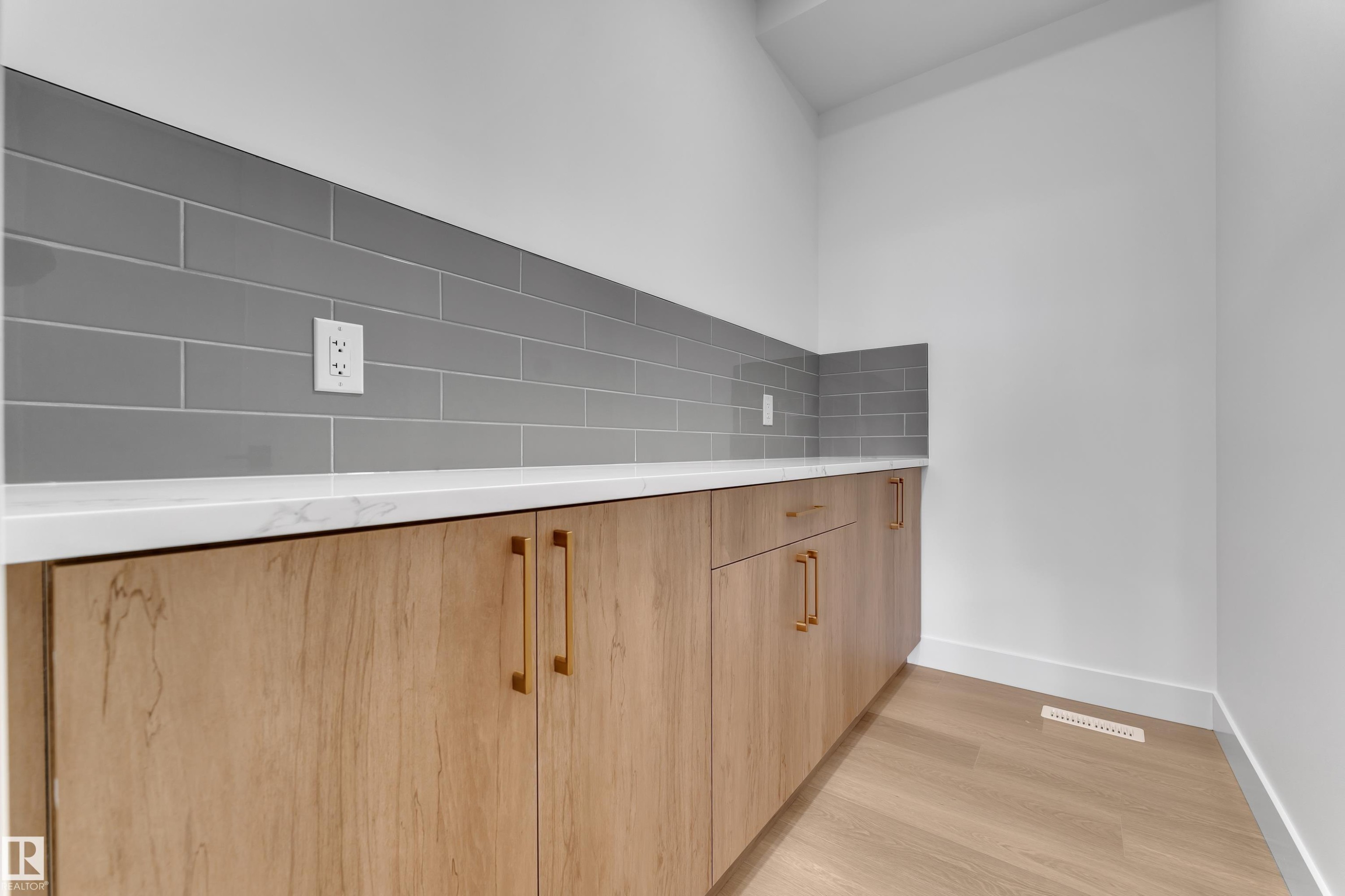 Wood-finish cabinetry with golden hardware, white countertop, grey subway tile backsplash, and wood-finish flooring - 794 Bank Drive, Leduc, AB
