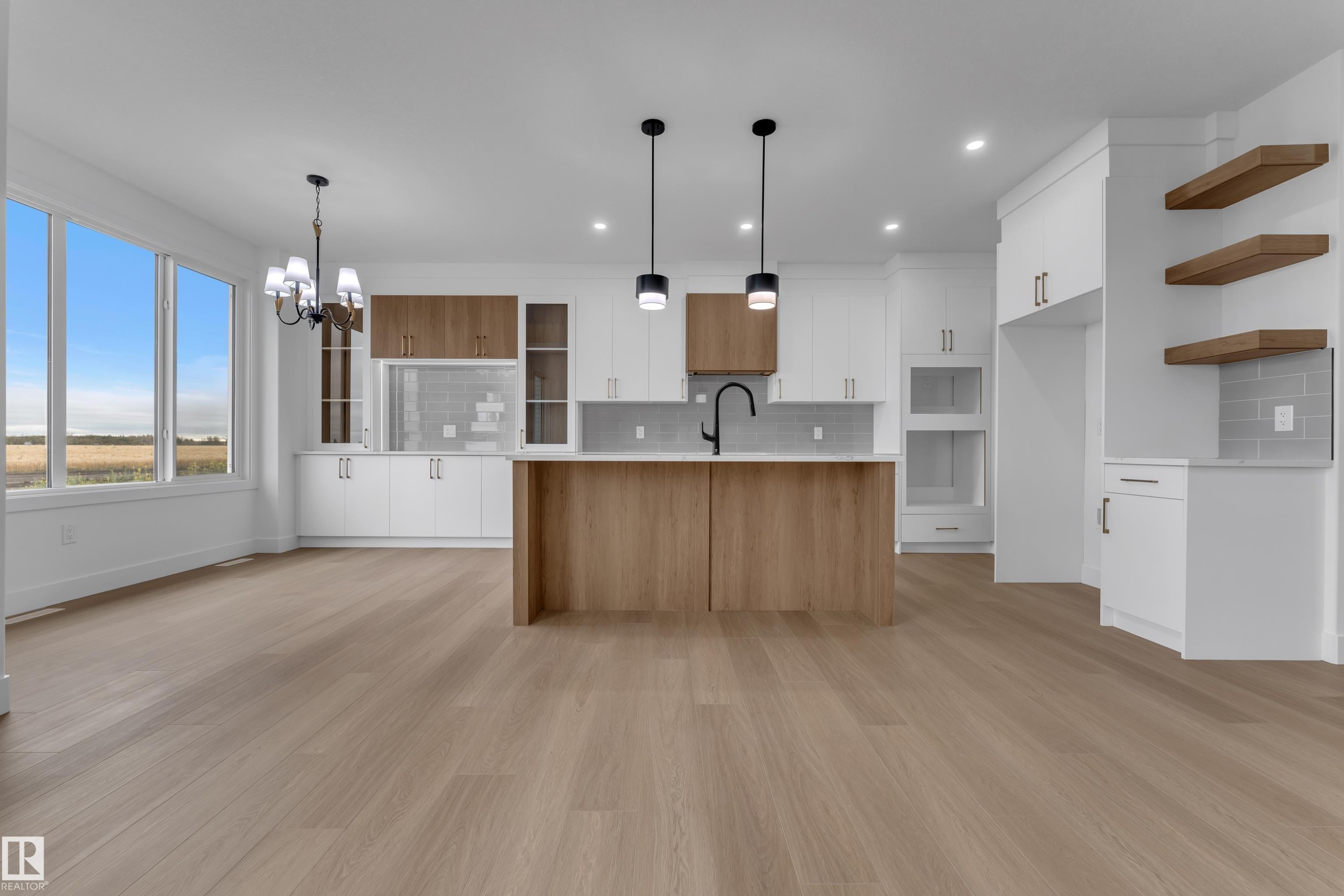 Bright kitchen featuring a central island with an undermount sink, pendant lighting, built-in appliances, and wood-finish flooring - 794 Bank Drive, Leduc, AB