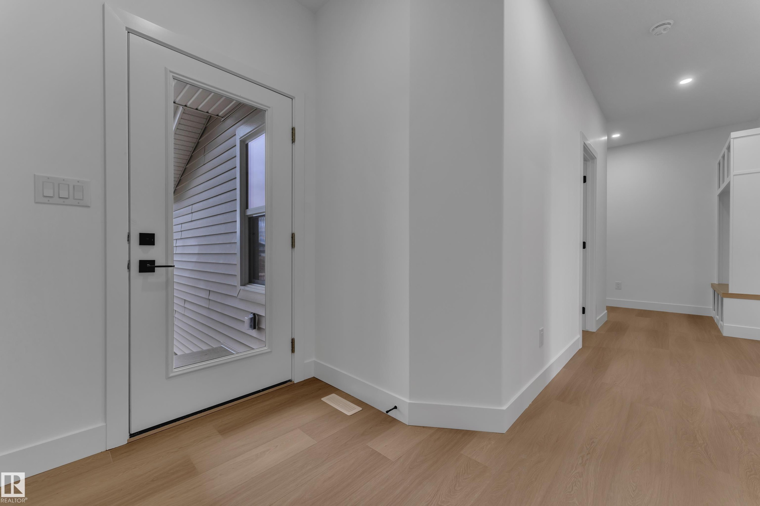 Light wood-finish flooring, recessed lighting, white walls, built-in storage bench, and a white door with a clear glass panel - 794 Bank Drive, Leduc, AB