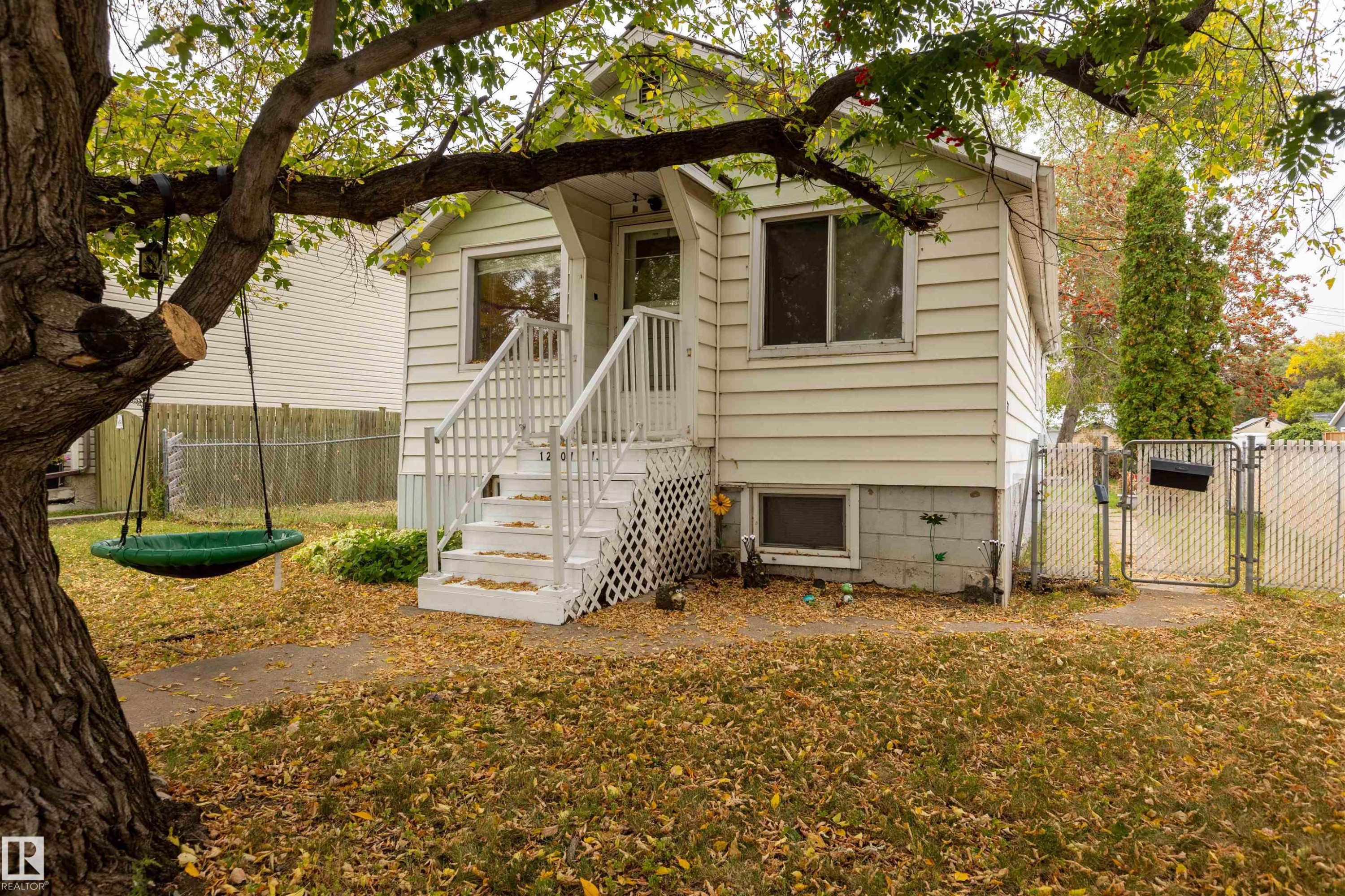 Wood siding exterior with white trim, a front porch featuring white railings and steps, and a chain-link fence - 12707 73 Street Nw, Edmonton, AB