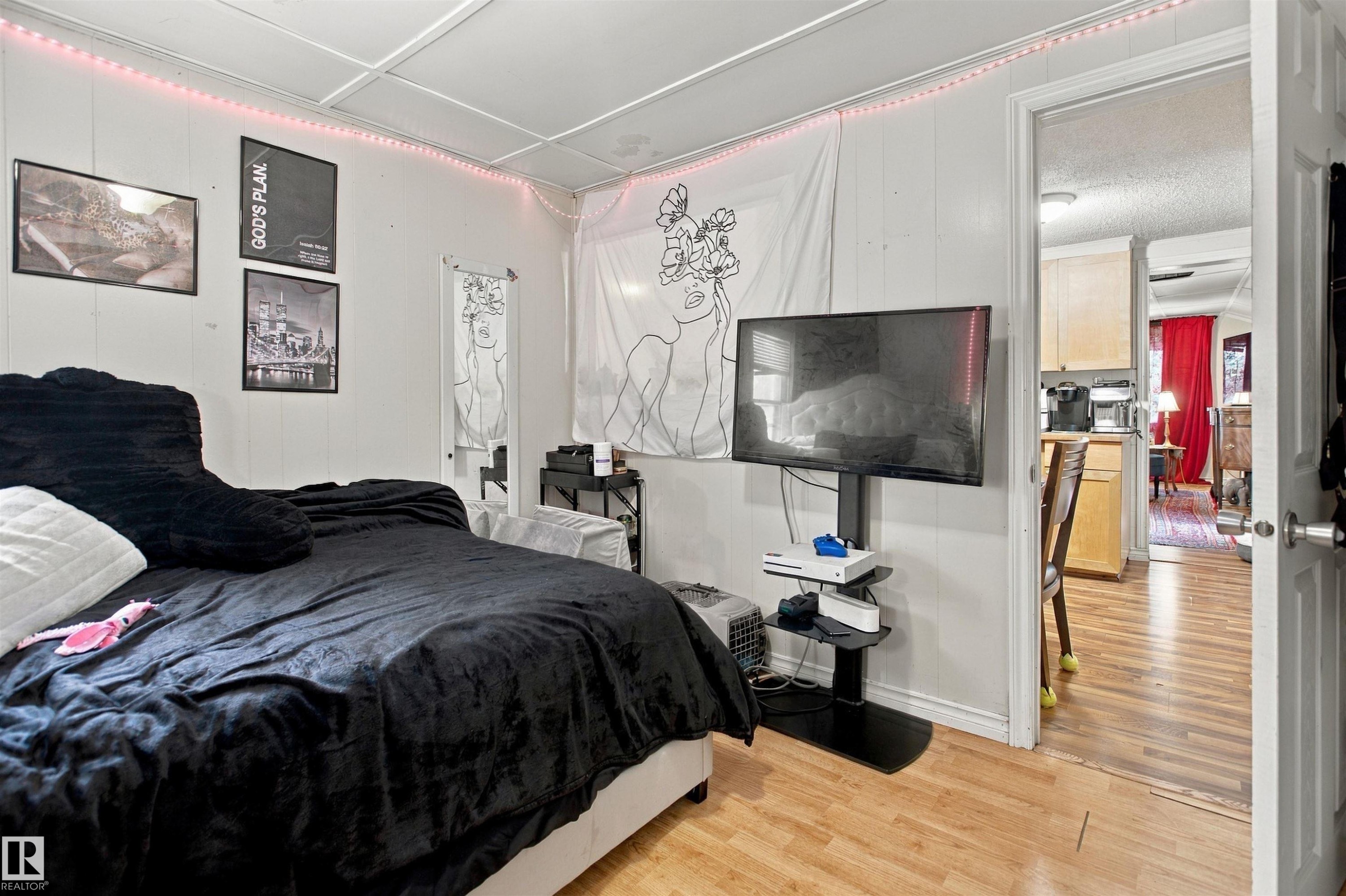 Spacious bedroom with wood-finish flooring, accent wall with artistic mural, and built-in media console with mounted flat-screen television - 12707 73 Street Nw, Edmonton, AB