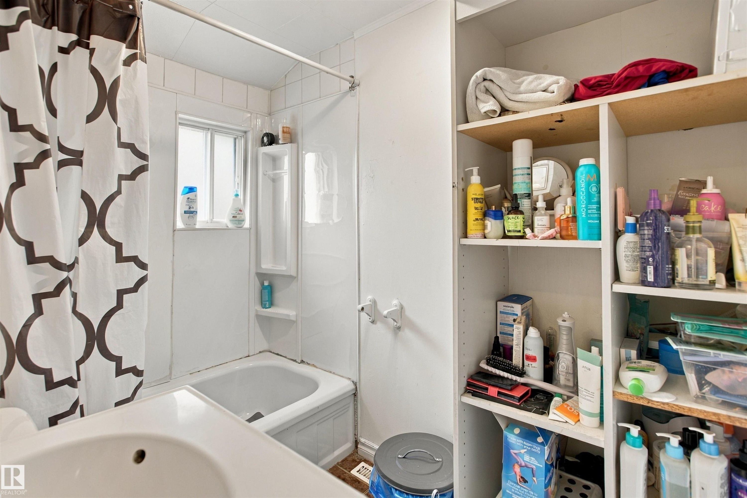 Bathroom featuring a spacious walk-in shower with geometric patterned curtain, pedestal sink, and extensive built-in cabinetry with wood-finish shelving - 12707 73 Street Nw, Edmonton, AB
