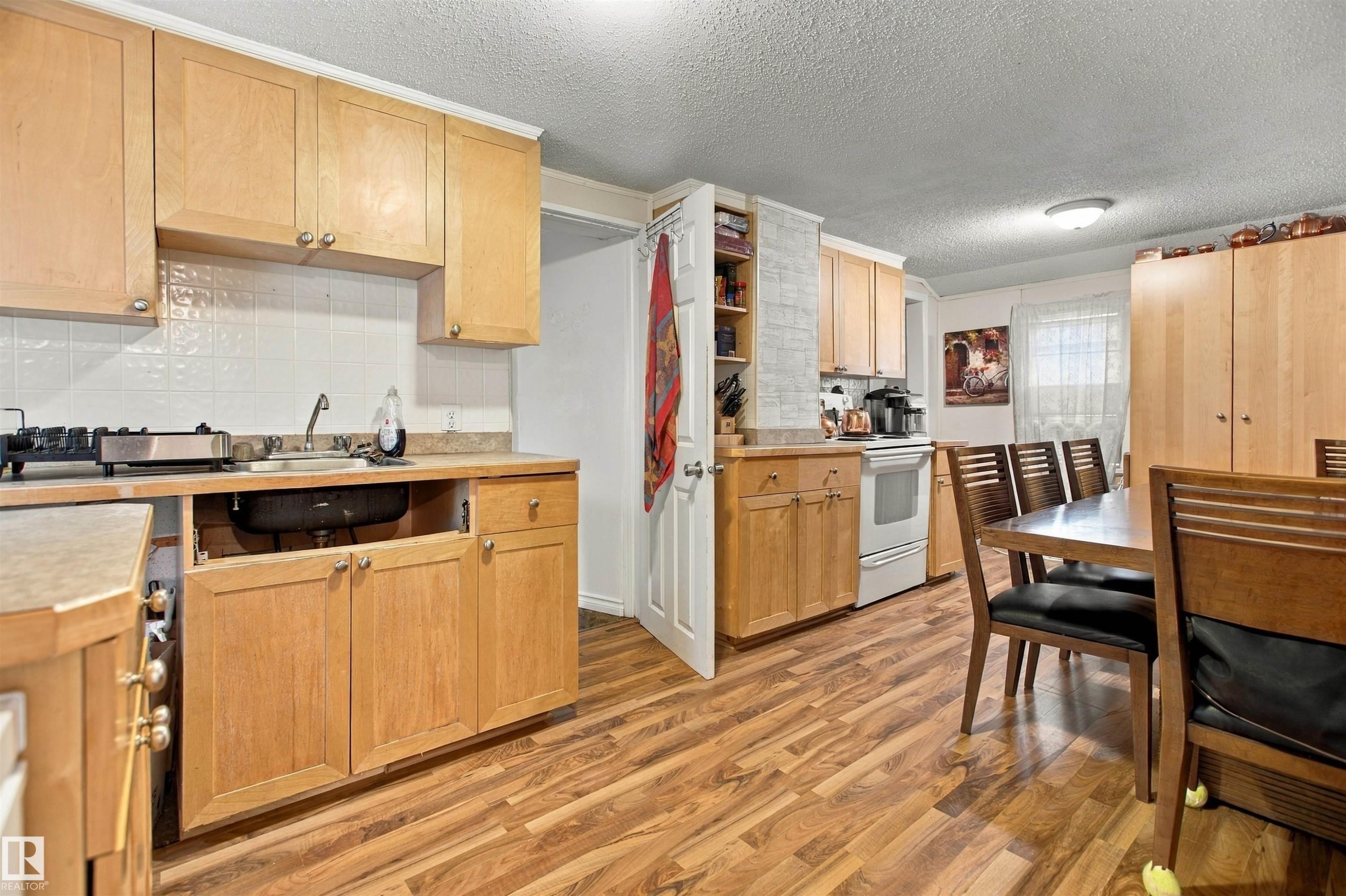 Wood-finish flooring throughout, light wood-tone cabinetry, white subway tile backsplash, recessed shelving, and a dining area - 12707 73 Street Nw, Edmonton, AB