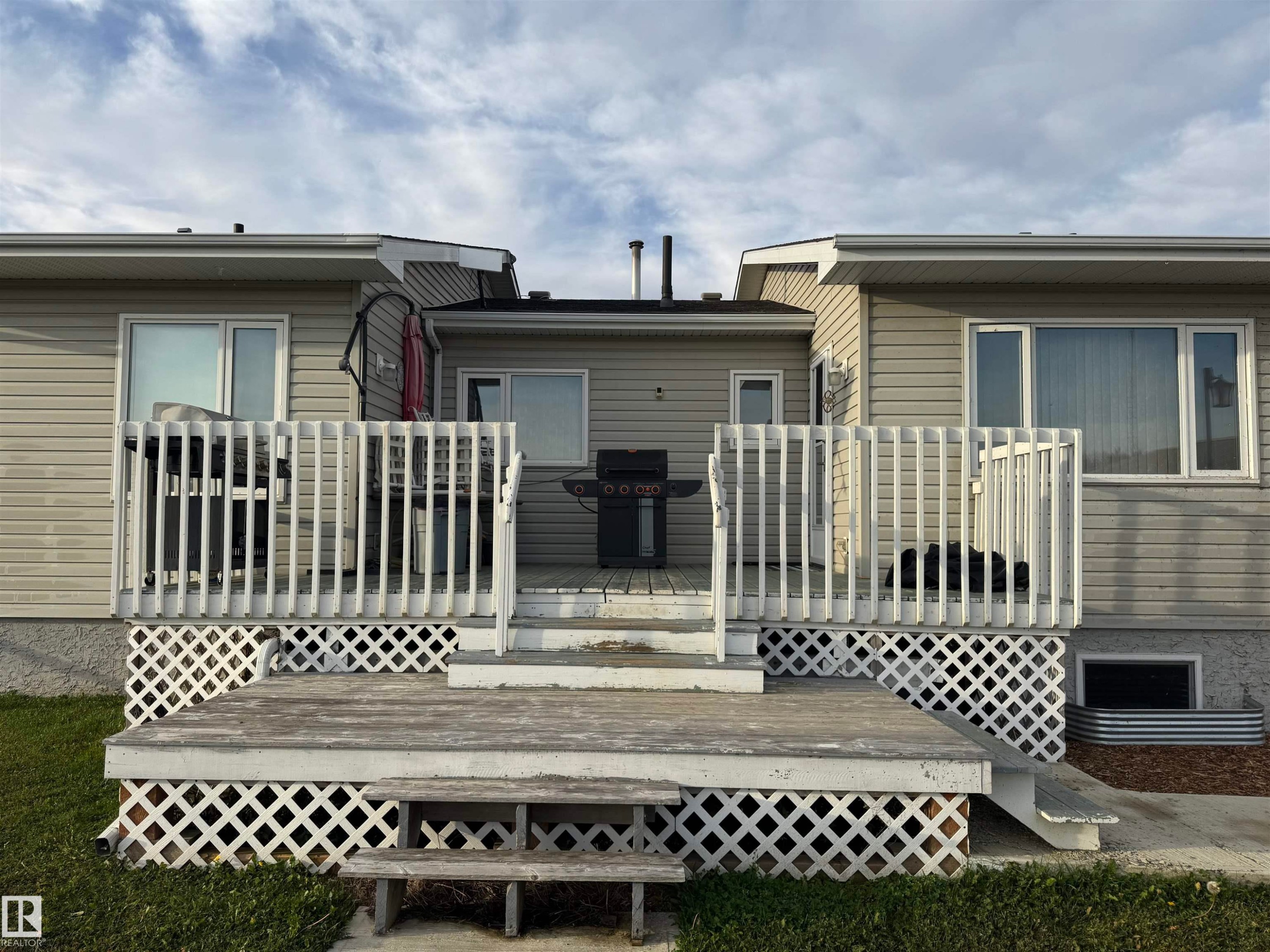 Multi-level wooden deck with lattice skirting, featuring white railings and dual-pane windows - 20120 Twp Rd 515, Rural Beaver County, AB