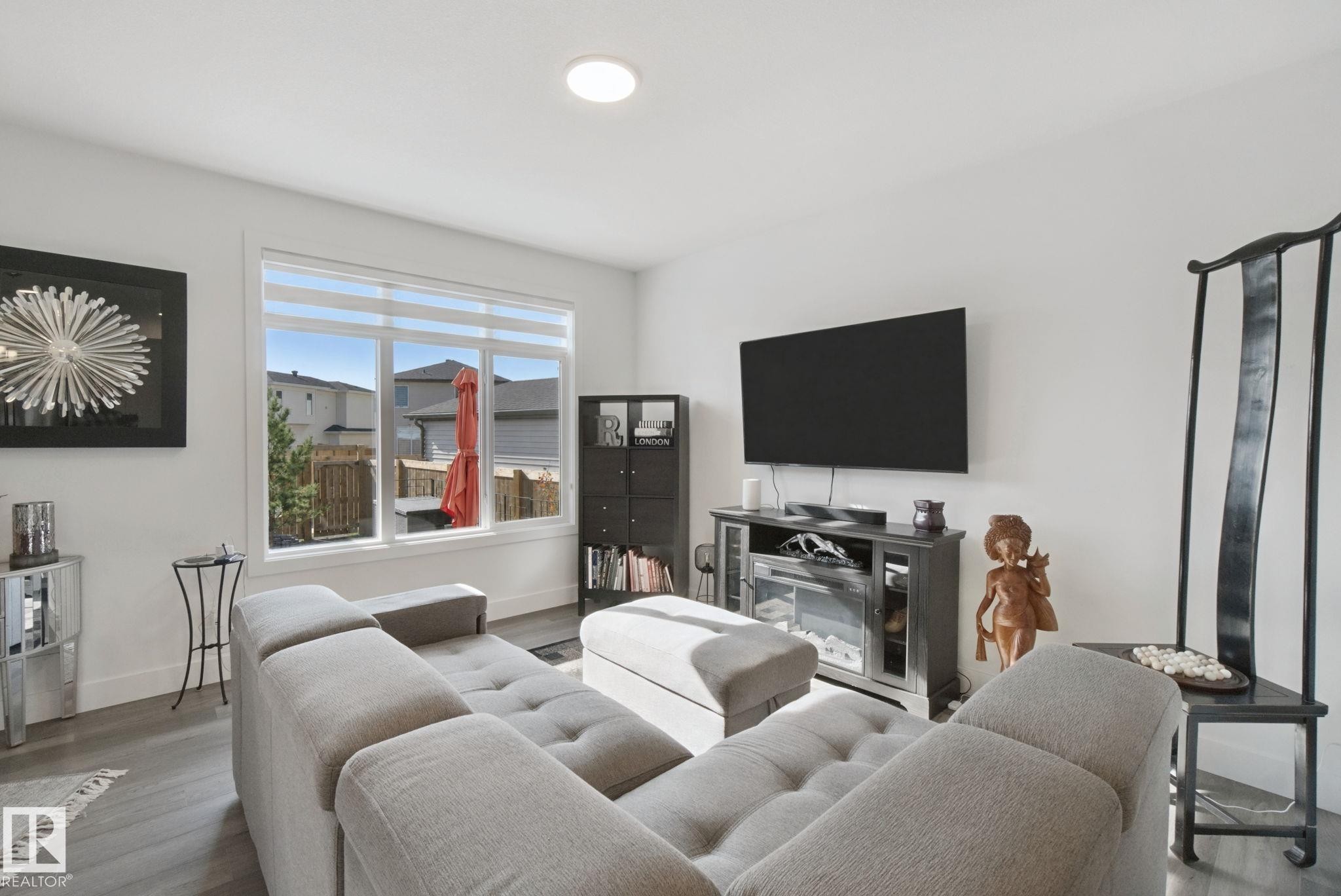 Expansive window with dual-layer blinds, recessed ceiling lighting, wood-finish flooring, and a built-in media console - 153 Cavanagh Common Sw, Edmonton, AB