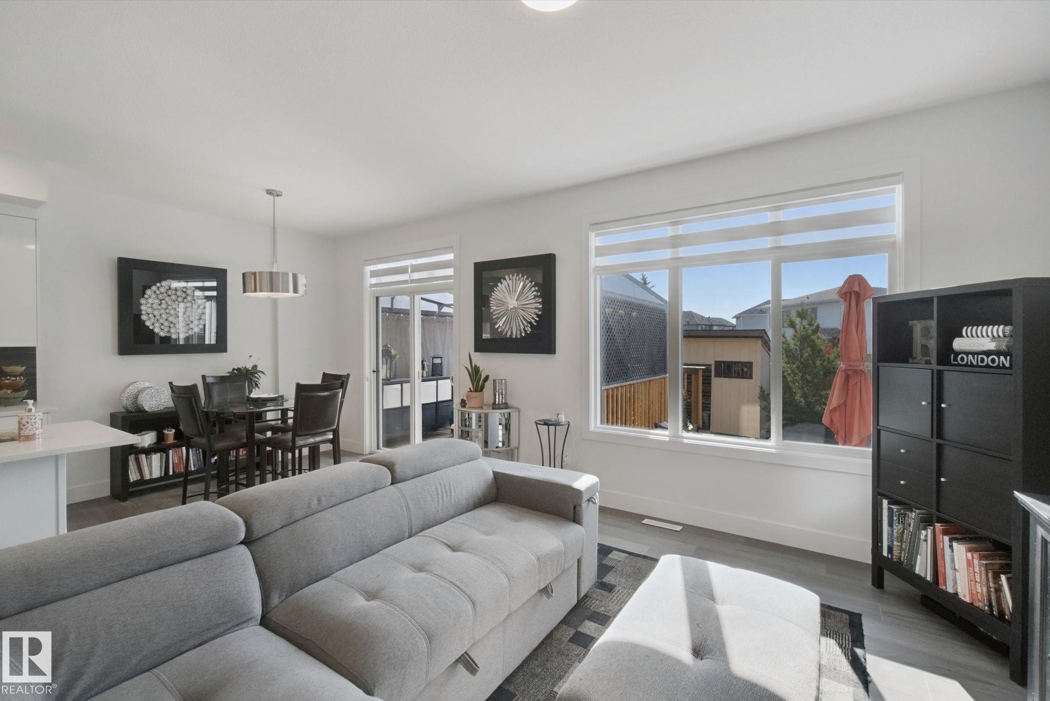 Open-concept living area with wood-finish flooring, large windows, and a sliding glass door - 153 Cavanagh Common Sw, Edmonton, AB