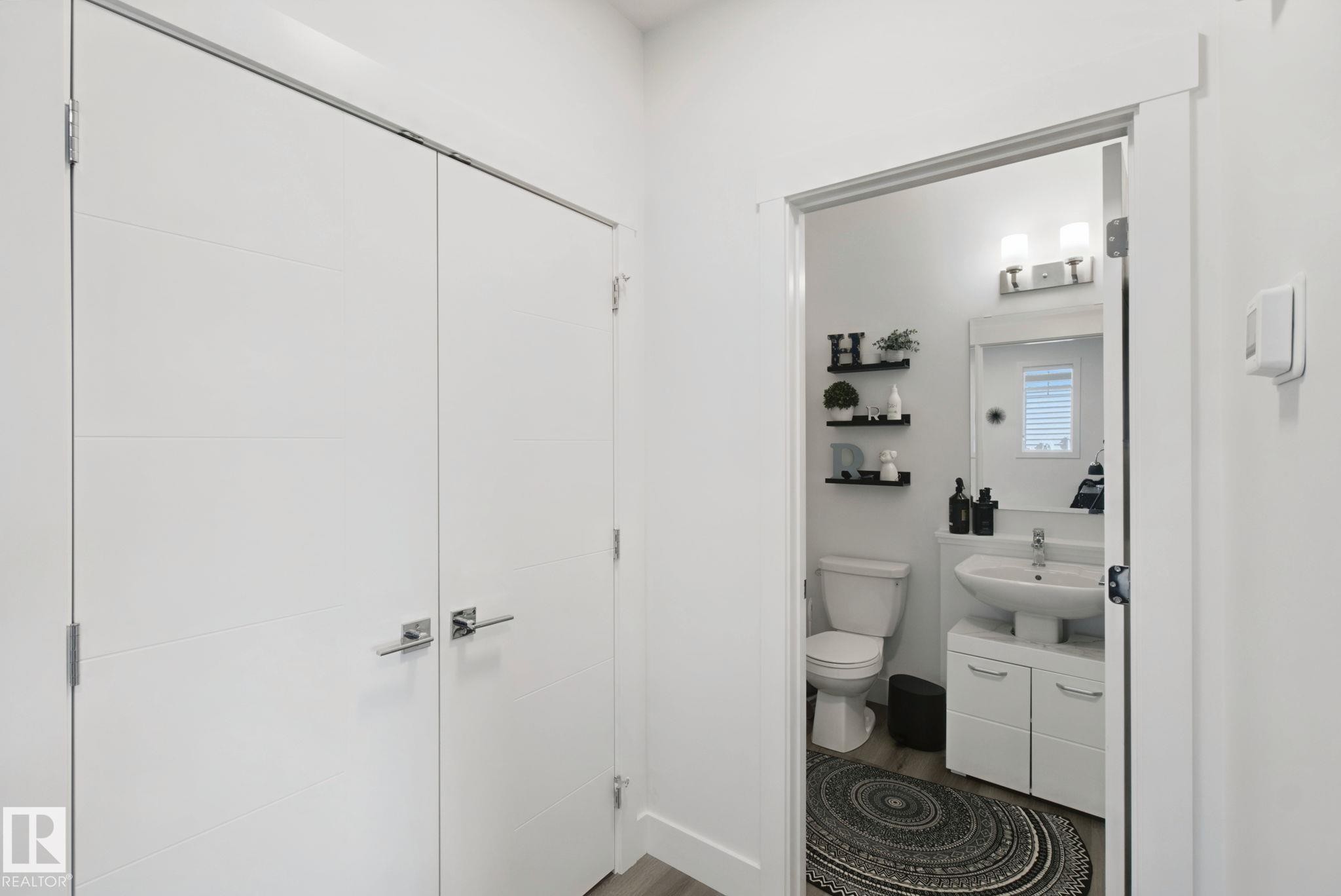 Recessed lighting, wood-finish flooring, white paneled doors with chrome hardware, white vanity with integrated sink, and wall-mounted light fixture - 153 Cavanagh Common Sw, Edmonton, AB