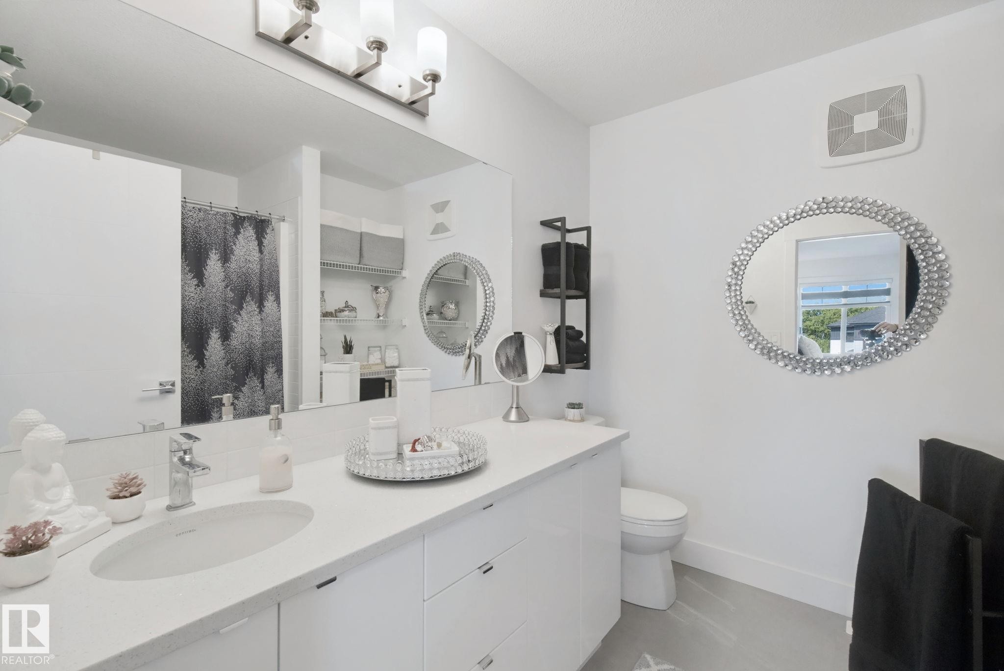 Dual vanity with undermount sinks, wall-mounted light fixture, large wall mirror, and built-in shelving - 153 Cavanagh Common Sw, Edmonton, AB