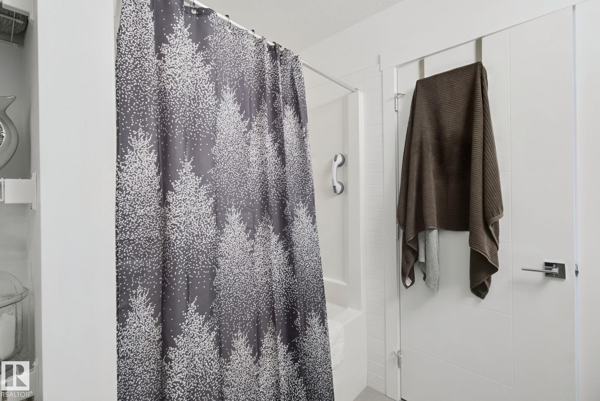 Shower enclosure with a white grab bar and a modern white door featuring a chrome lever handle - 153 Cavanagh Common Sw, Edmonton, AB