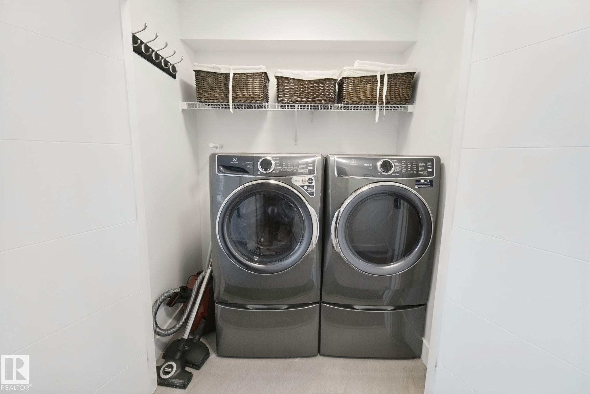 Dedicated laundry area featuring front-loading washer and dryer, elevated on pedestals - 153 Cavanagh Common Sw, Edmonton, AB