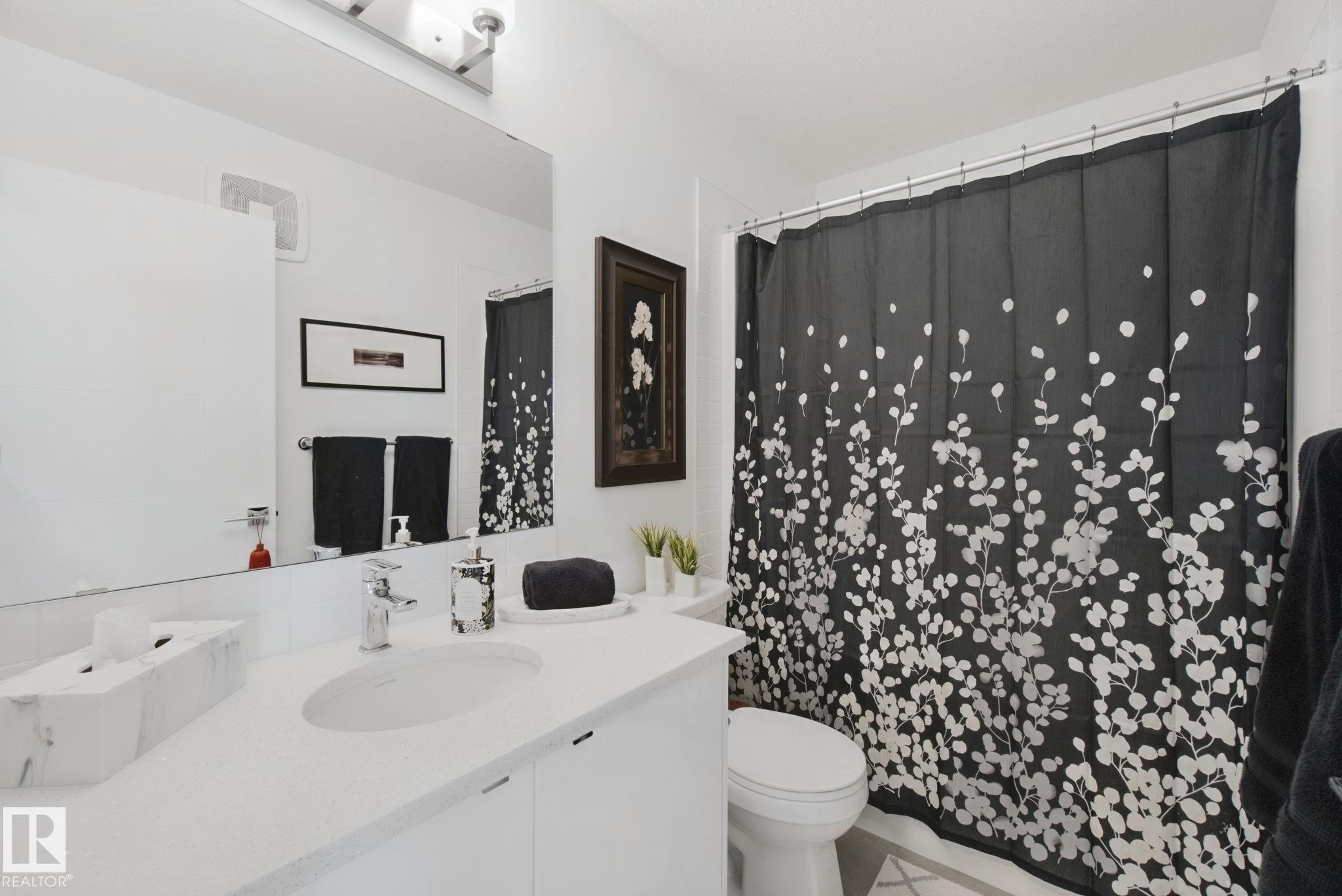 White vanity with integrated sink, chrome faucet, wall-mounted mirror, and overhead light fixture - 153 Cavanagh Common Sw, Edmonton, AB