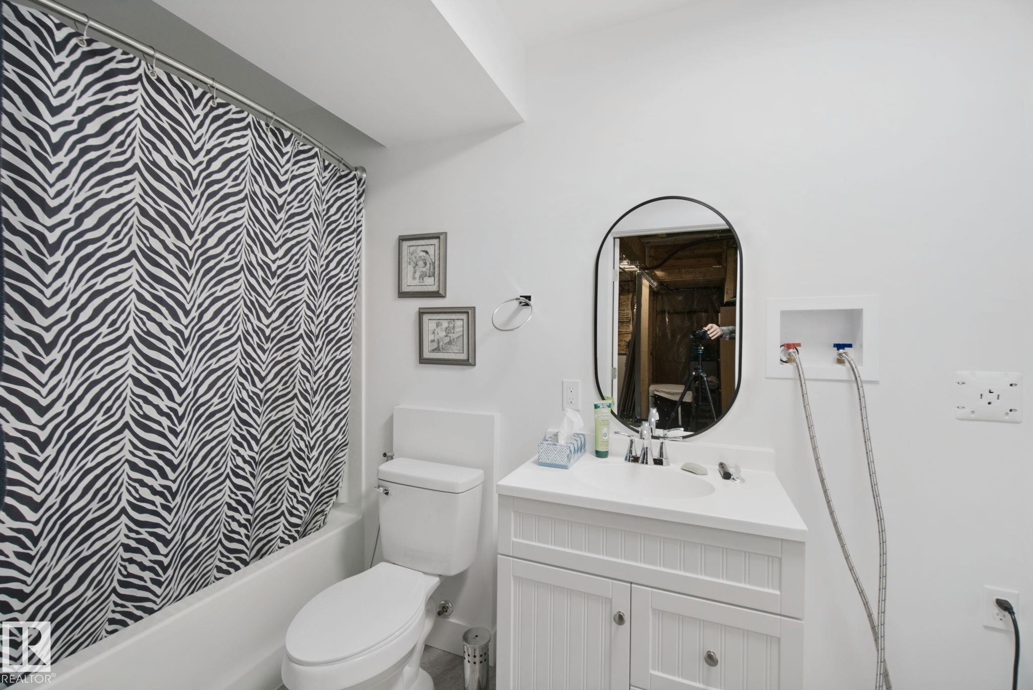 Bathroom featuring a white vanity with integrated sink, oval mirror, bathtub with shower, and toilet - 153 Cavanagh Common Sw, Edmonton, AB
