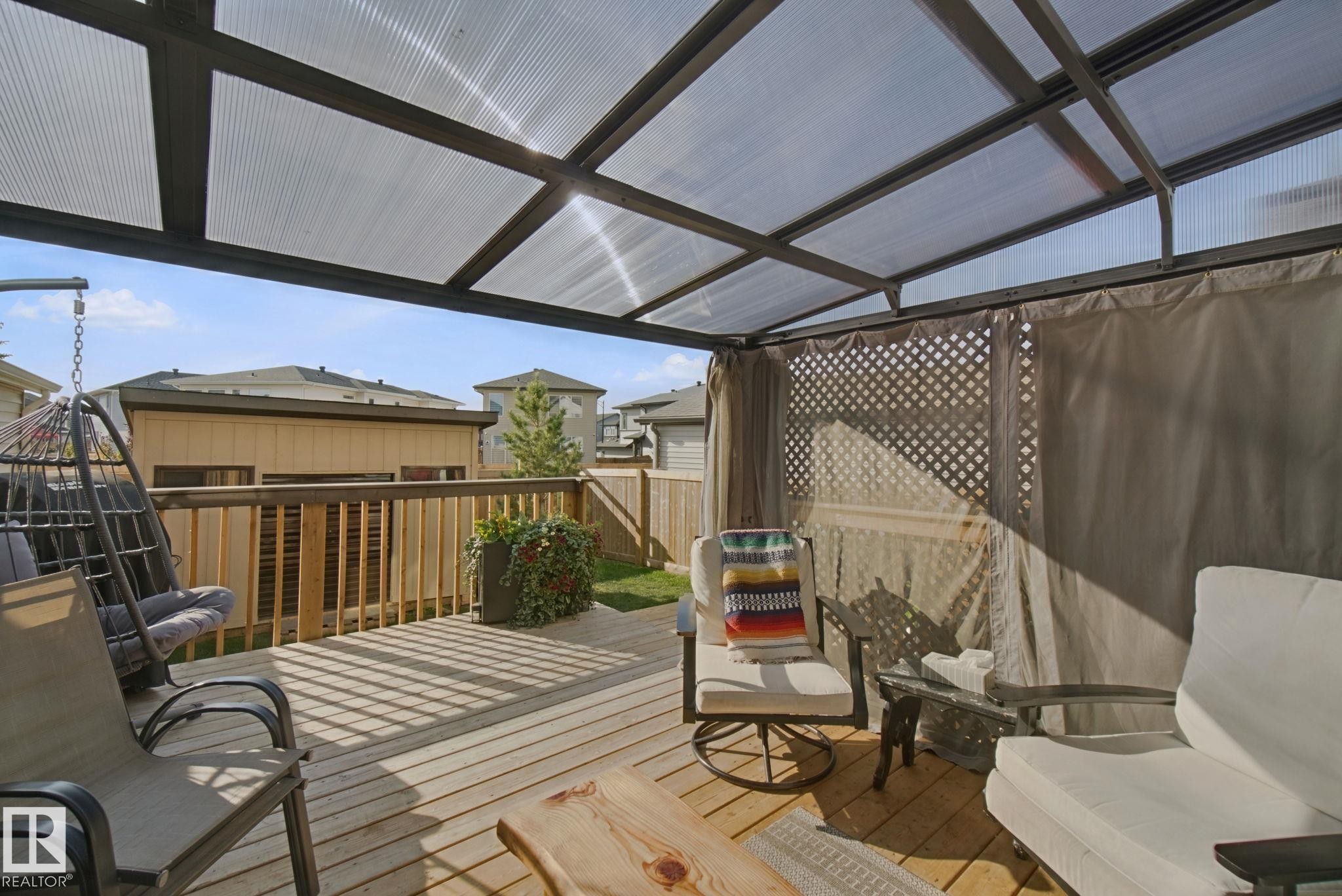 Wood-finish deck with a transparent roof structure, lattice privacy screen, and a surrounding wood fence - 153 Cavanagh Common Sw, Edmonton, AB