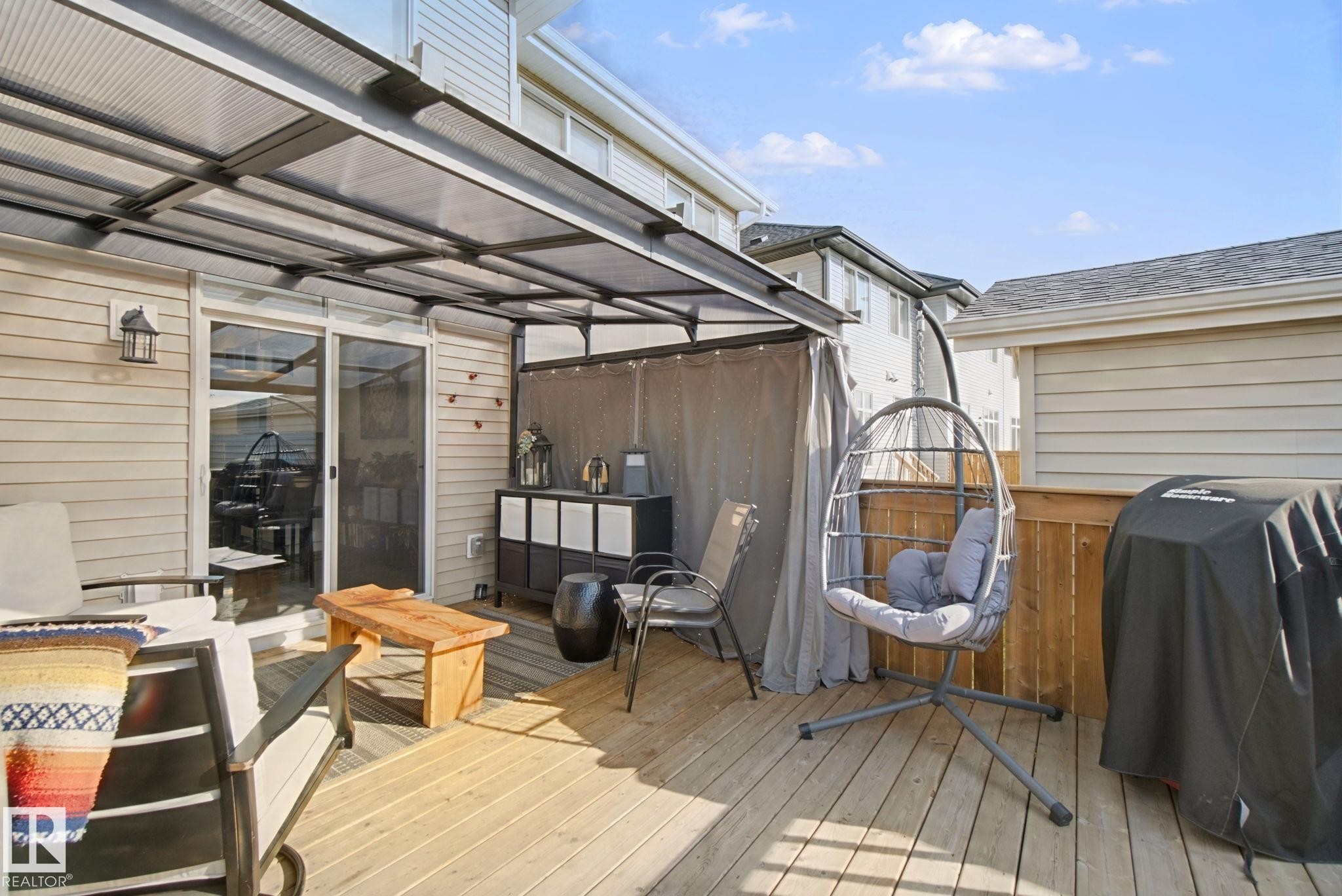 Expansive wood-finish deck with a clear panel awning, sliding glass door entry, and wood privacy fencing - 153 Cavanagh Common Sw, Edmonton, AB