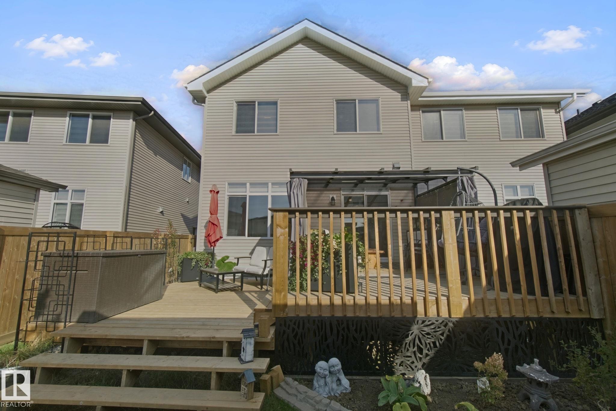 Expansive wood-finish deck with integrated hot tub, privacy fence, and a pergola structure - 153 Cavanagh Common Sw, Edmonton, AB