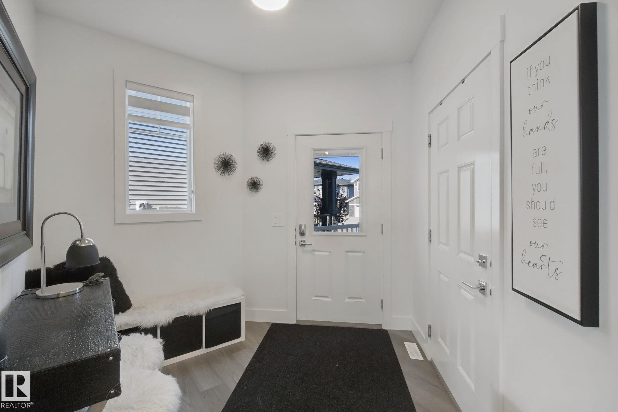 Bright entry featuring wood-finish flooring, a white paneled door with frosted glass, and a second white paneled door - 153 Cavanagh Common Sw, Edmonton, AB