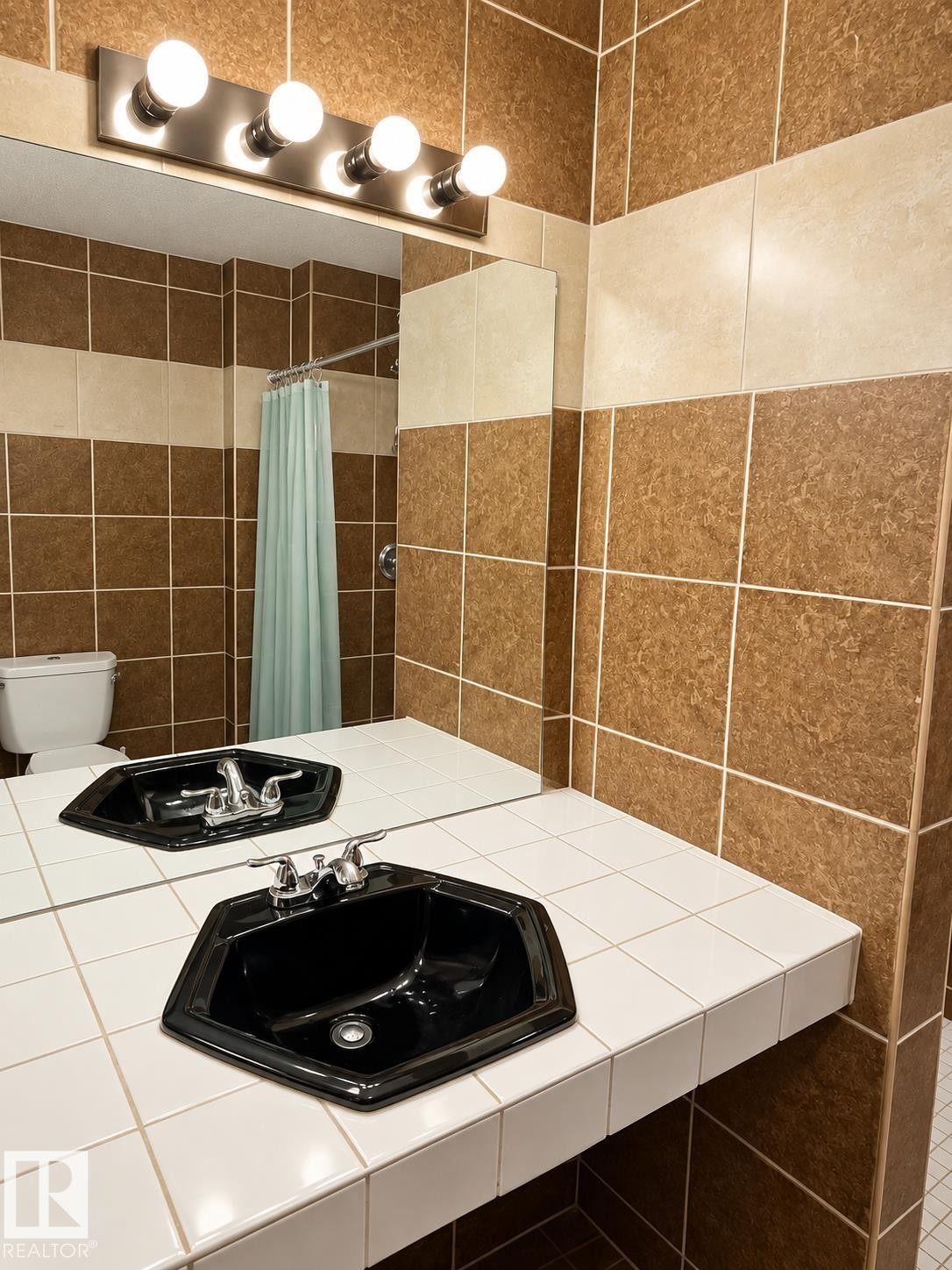 Two-tone tiled walls, a full-width mirror, a five-bulb vanity light, a built-in tiled countertop, and an octagonal basin with chrome fixtures - 18929 99A Avenue Nw, Edmonton, AB