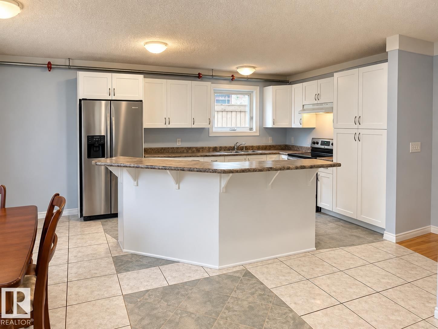 Kitchen featuring white cabinetry, a large kitchen island, stainless steel refrigerator, and a built-in range - 18929 99A Avenue Nw, Edmonton, AB