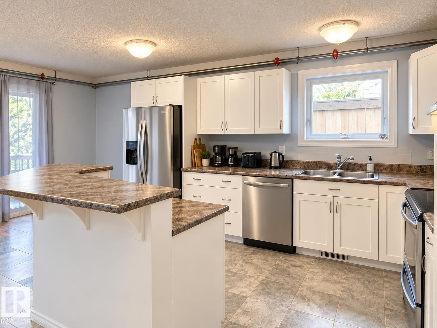 Kitchen featuring white cabinetry, stainless steel appliances, a double basin sink, a multi-level island, and tiled flooring - 18929 99A Avenue Nw, Edmonton, AB