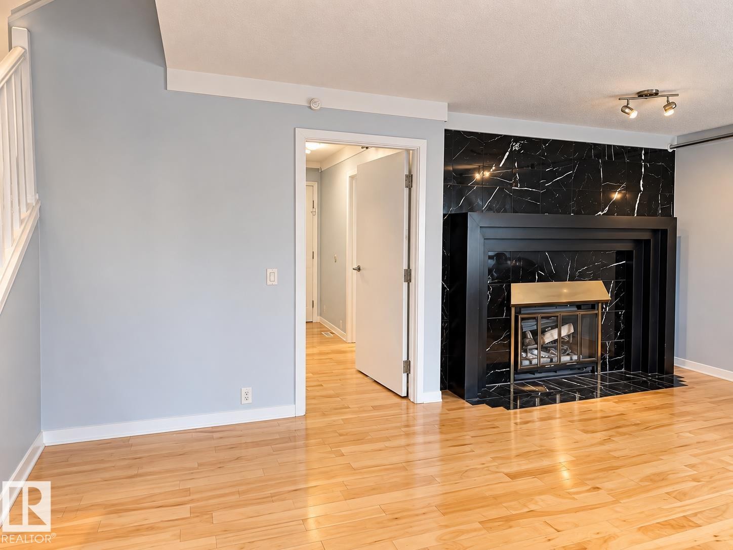 Hardwood flooring, black marble-look fireplace surround, integrated fireplace screen, white trim, and track lighting - 18929 99A Avenue Nw, Edmonton, AB
