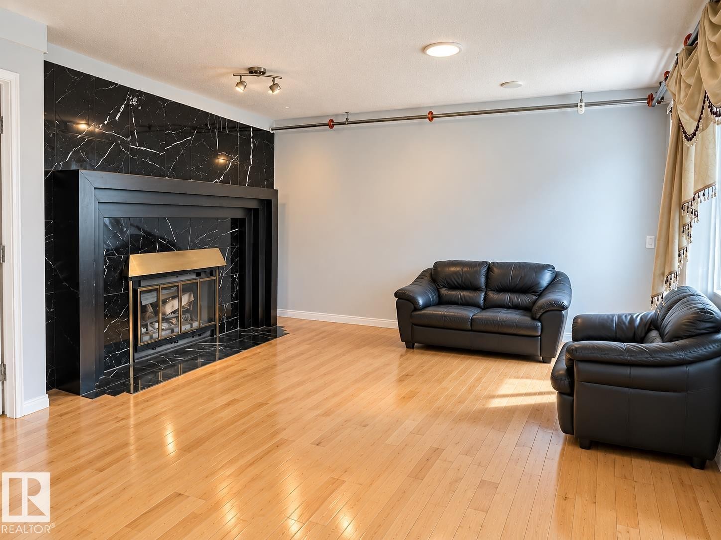 Hardwood flooring, black fireplace surround with black mantel, black marble-style wall paneling, and track lighting - 18929 99A Avenue Nw, Edmonton, AB