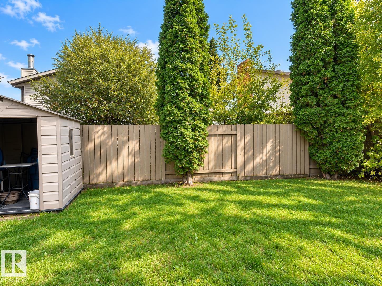 Spacious backyard featuring a manicured lawn, privacy fencing, mature trees, and a utility shed - 18929 99A Avenue Nw, Edmonton, AB