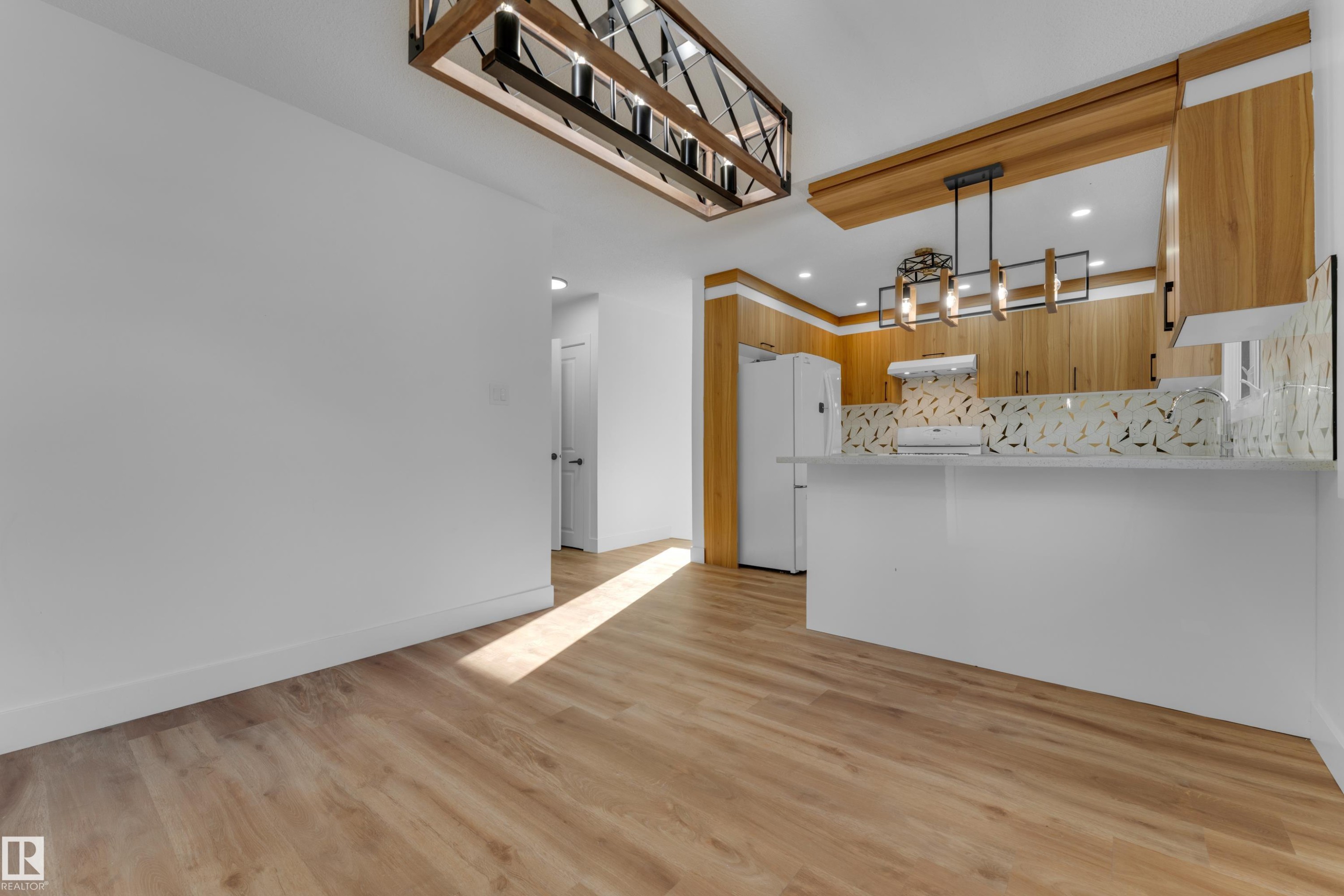Wood-finish flooring, white walls, kitchen island with a white countertop, wood cabinetry, and a geometric backsplash - 52314 Rge Road 215, Rural Strathcona County, AB