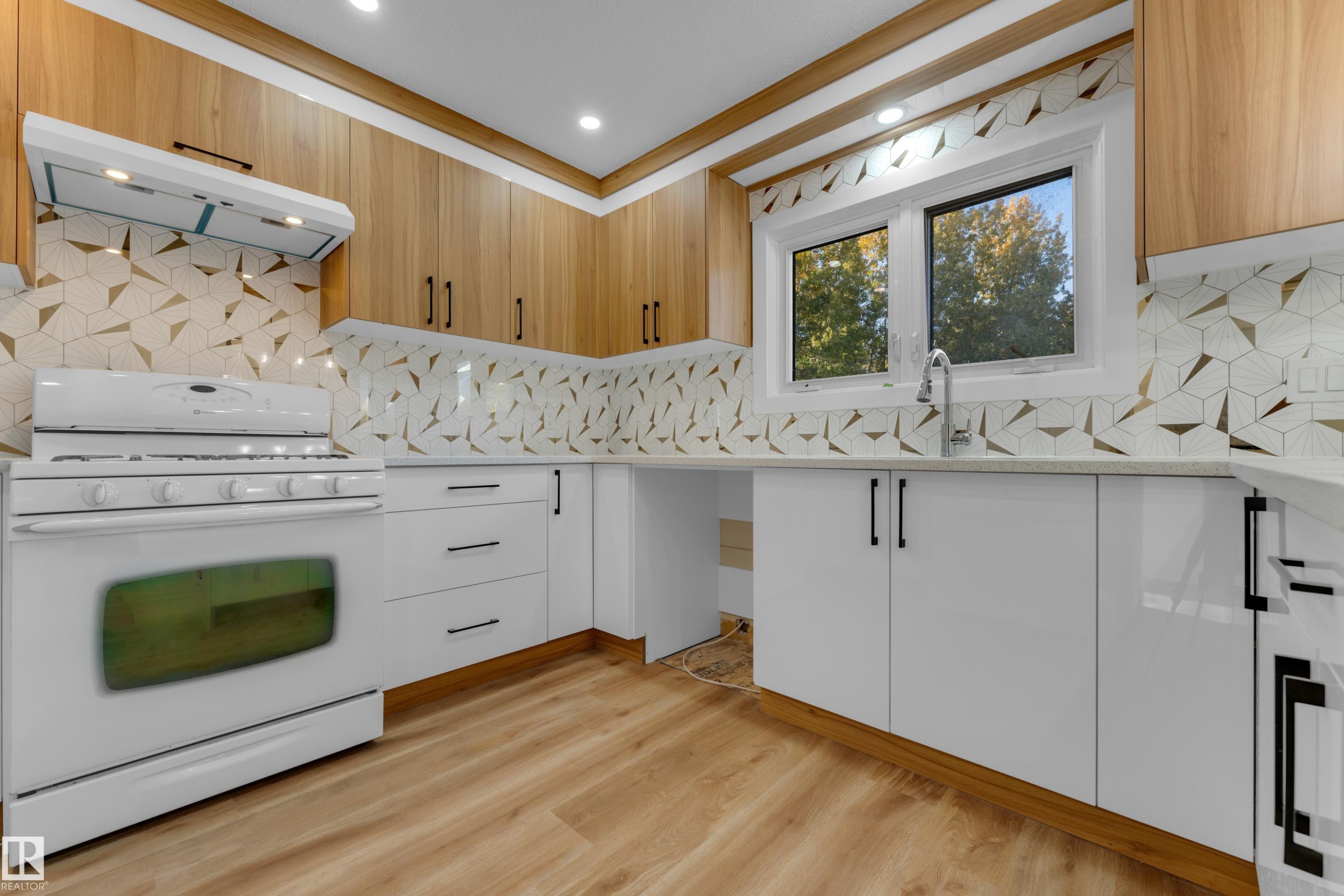 Wood-finish flooring, white cabinetry with matte black hardware, geometric pattern tile backsplash, light-toned countertops, and recessed lighting - 52314 Rge Road 215, Rural Strathcona County, AB