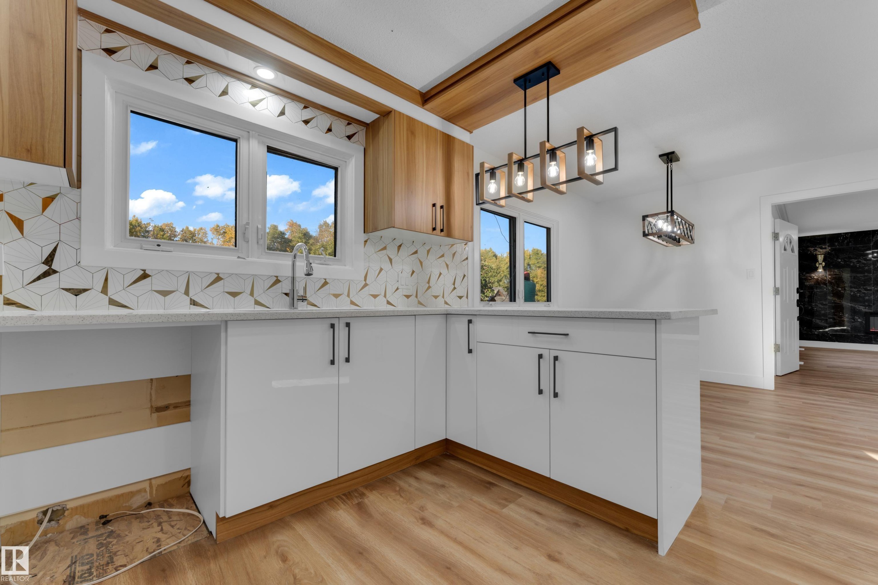 Contemporary kitchen featuring white cabinetry with black hardware, wood-finish flooring, a geometric tile backsplash, and a window above the sink - 52314 Rge Road 215, Rural Strathcona County, AB