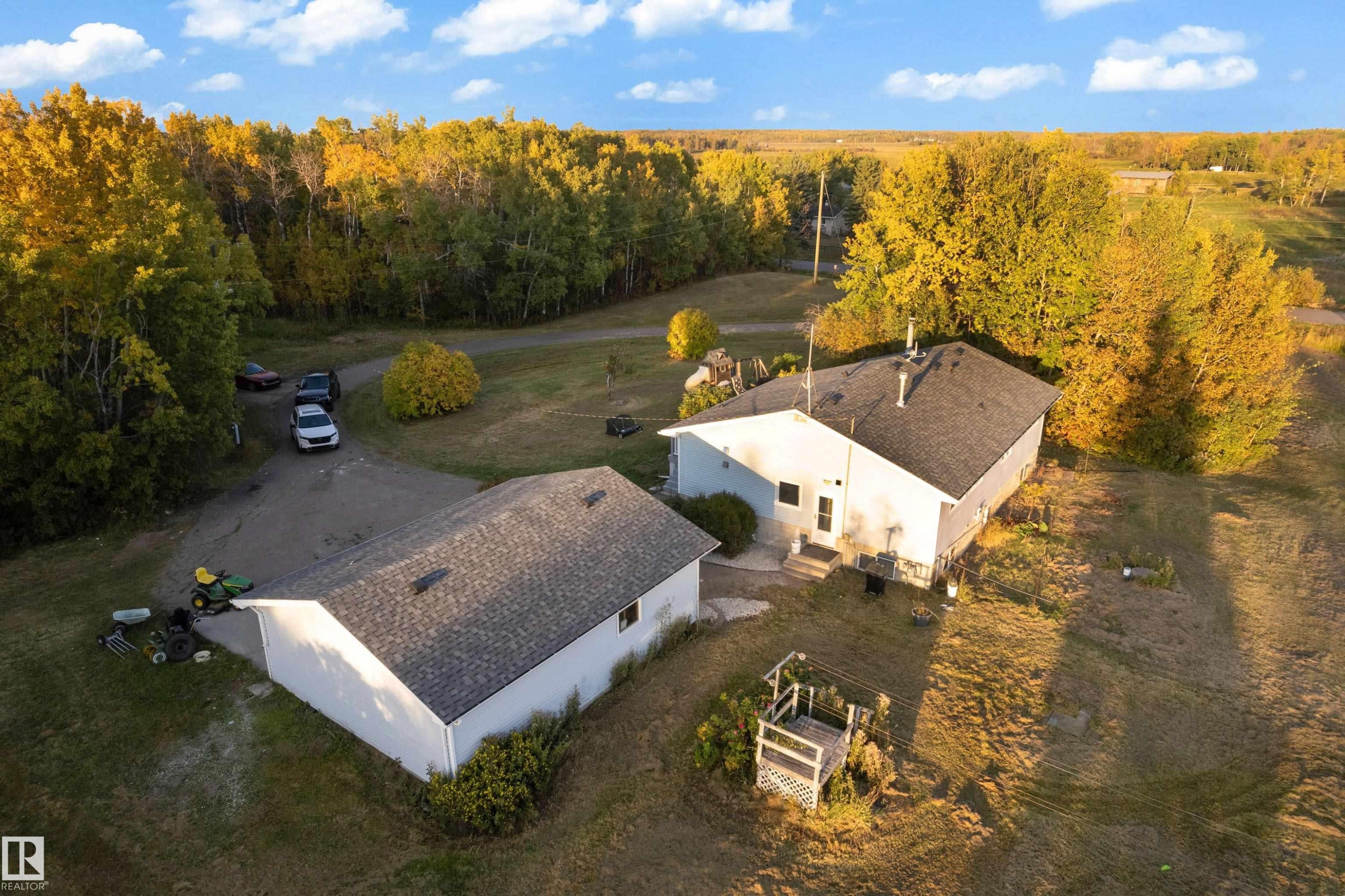 Spacious property featuring a main residence with a dark shingle roof, a detached ancillary building with a matching shingle roof, and a gravel driveway - 52314 Rge Road 215, Rural Strathcona County, AB