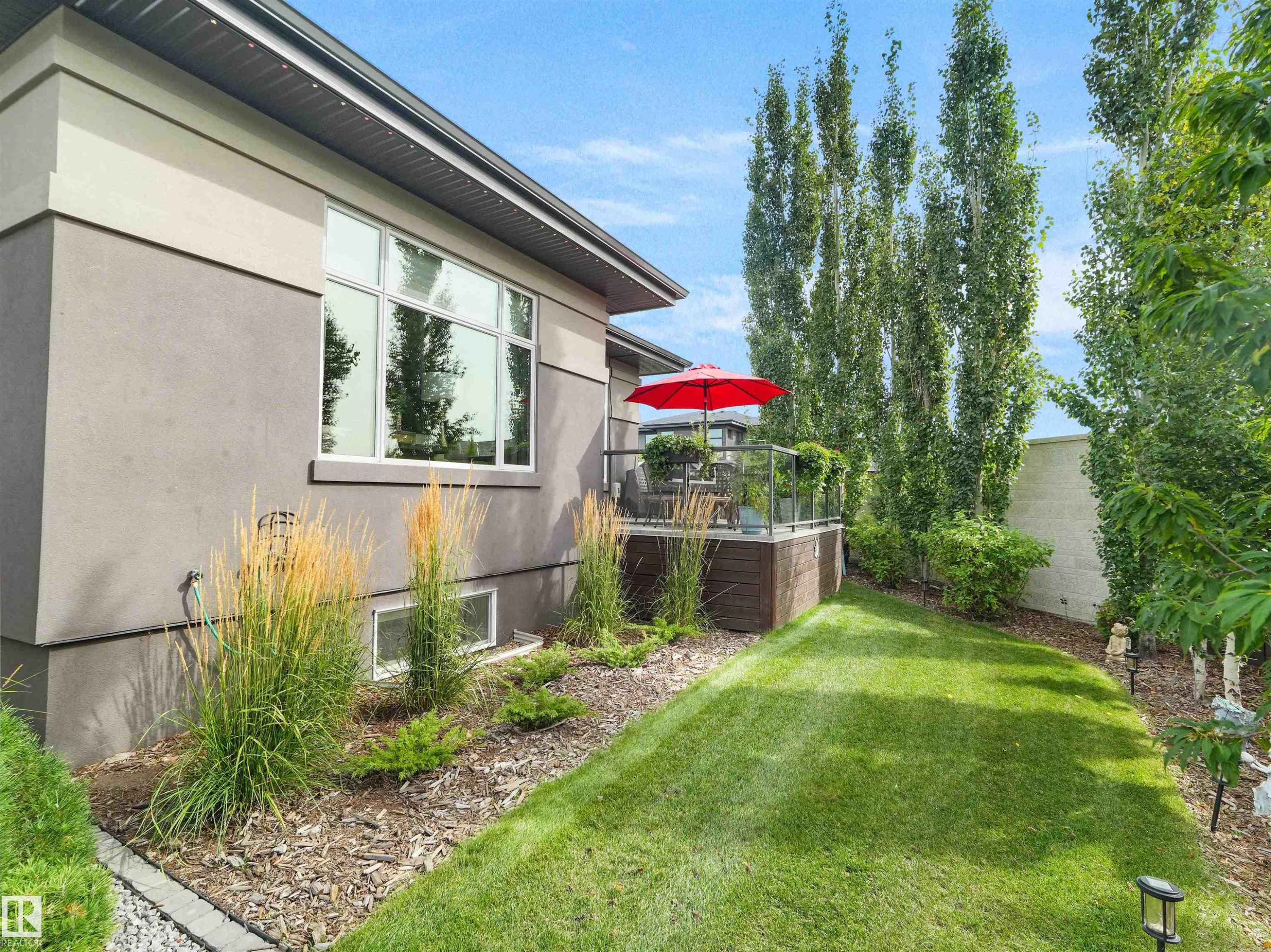 Exterior featuring stucco siding, a raised deck with glass railings, an expansive lawn, and mature trees - 904 Wood Place Nw, Edmonton, AB