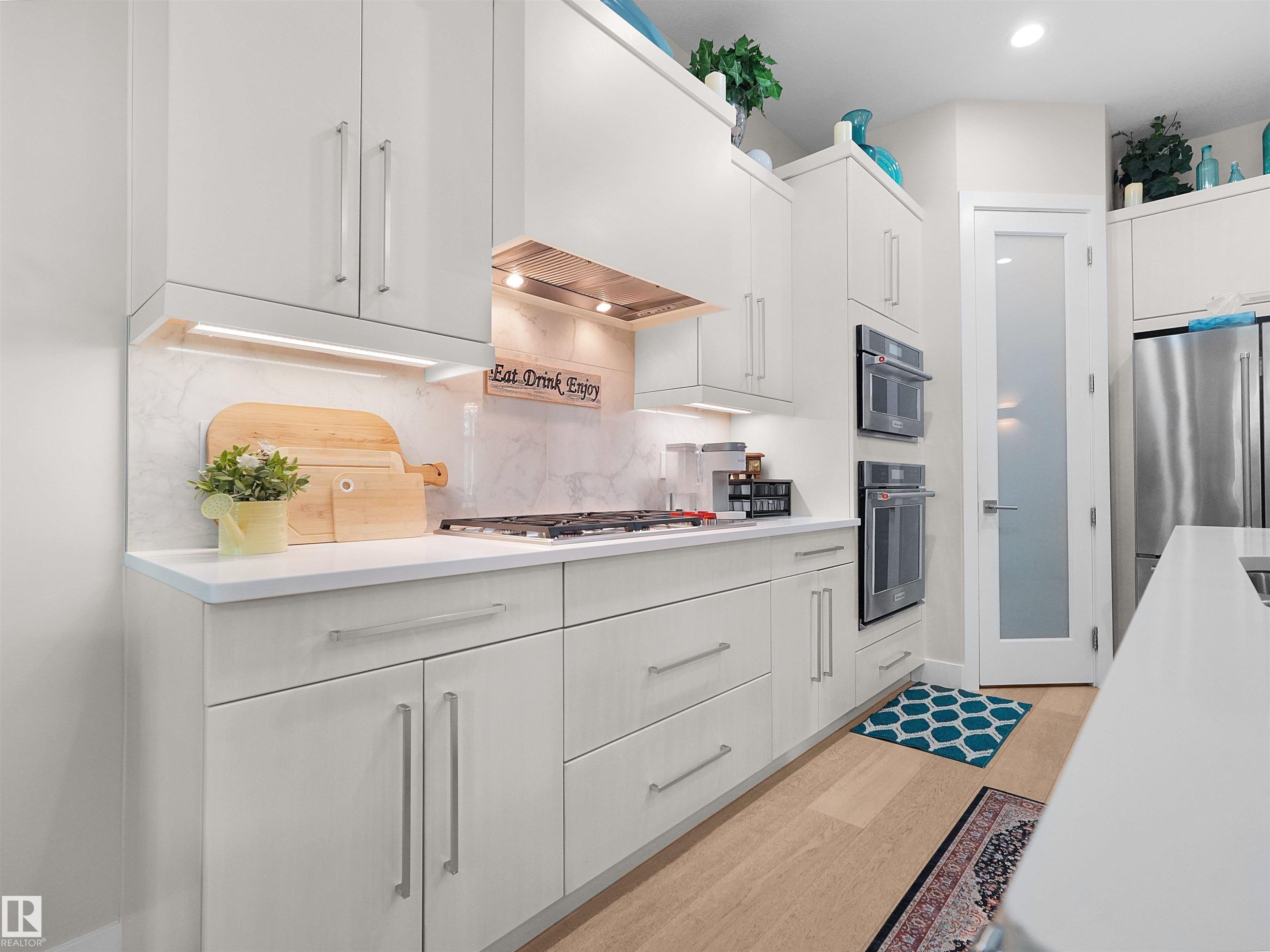 Contemporary kitchen featuring light wood-finish flooring, white cabinetry with silver-toned hardware, a light-toned countertop, a built-in oven, and a built-in microwave - 904 Wood Place Nw, Edmonton, AB