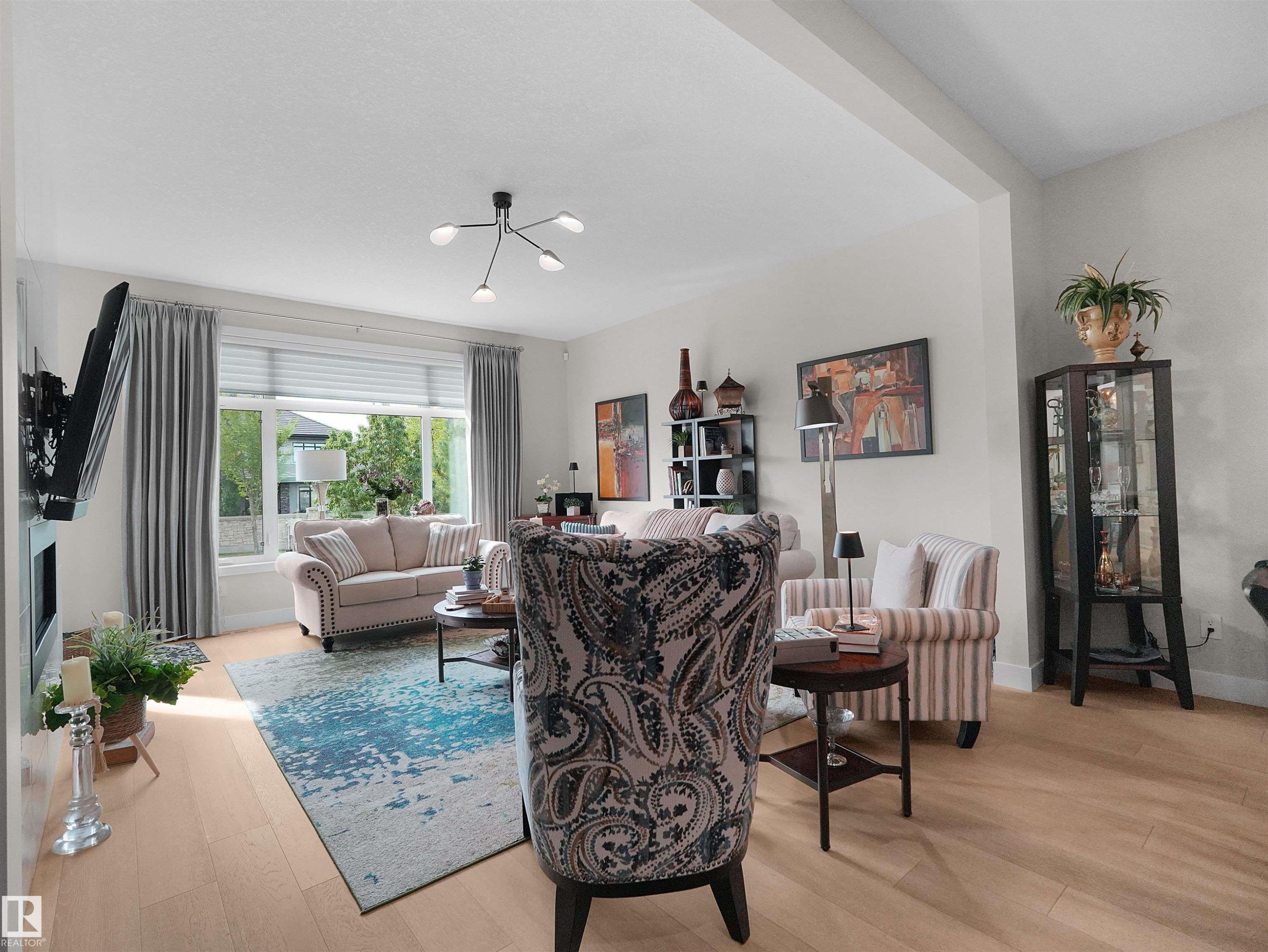 Bright living area featuring light wood-finish flooring, a large picture window, and a modern ceiling light fixture - 904 Wood Place Nw, Edmonton, AB