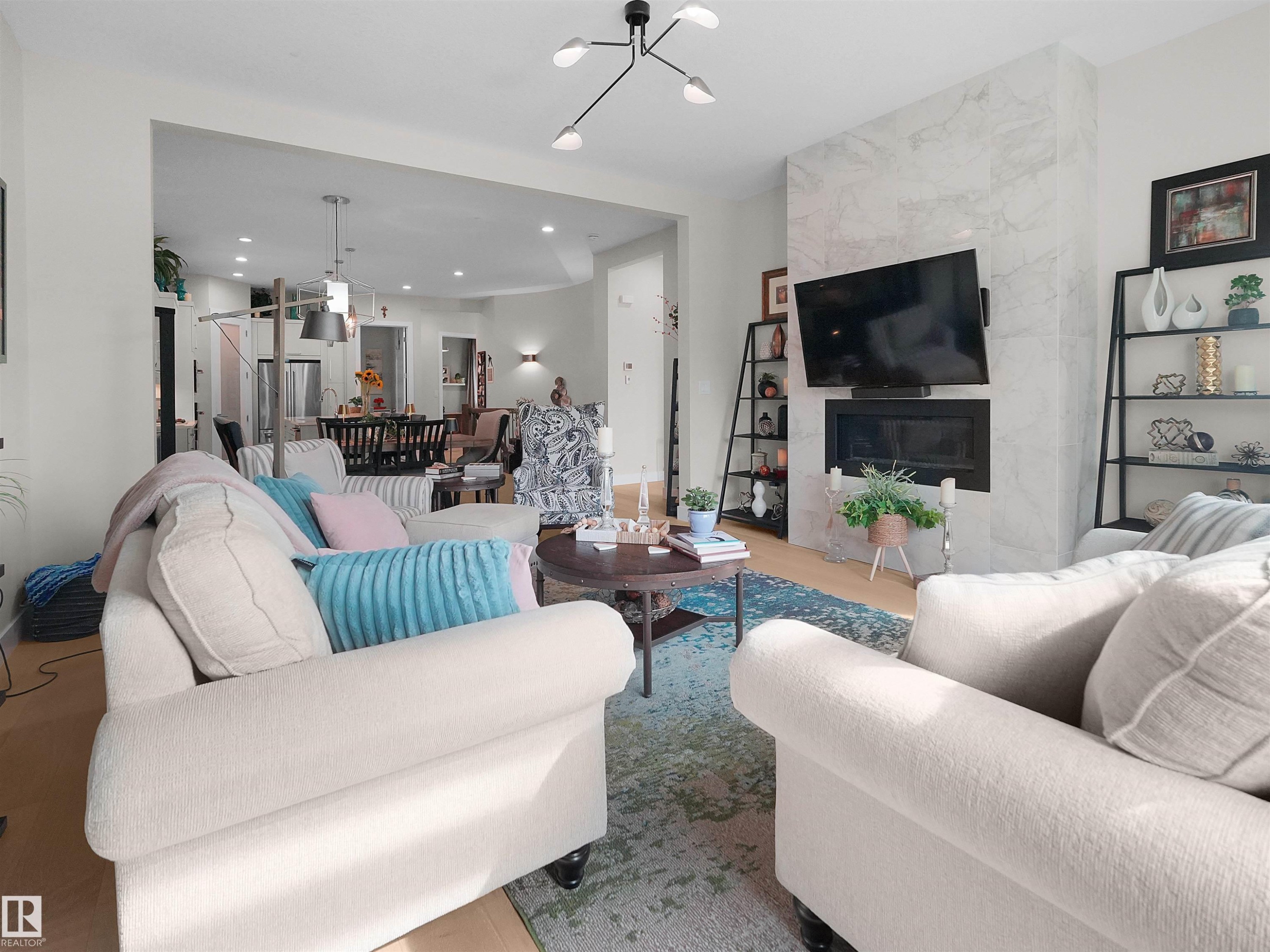 Open-concept living space featuring wood-finish flooring, a contemporary ceiling light fixture, and a fireplace with a stone-tile surround - 904 Wood Place Nw, Edmonton, AB