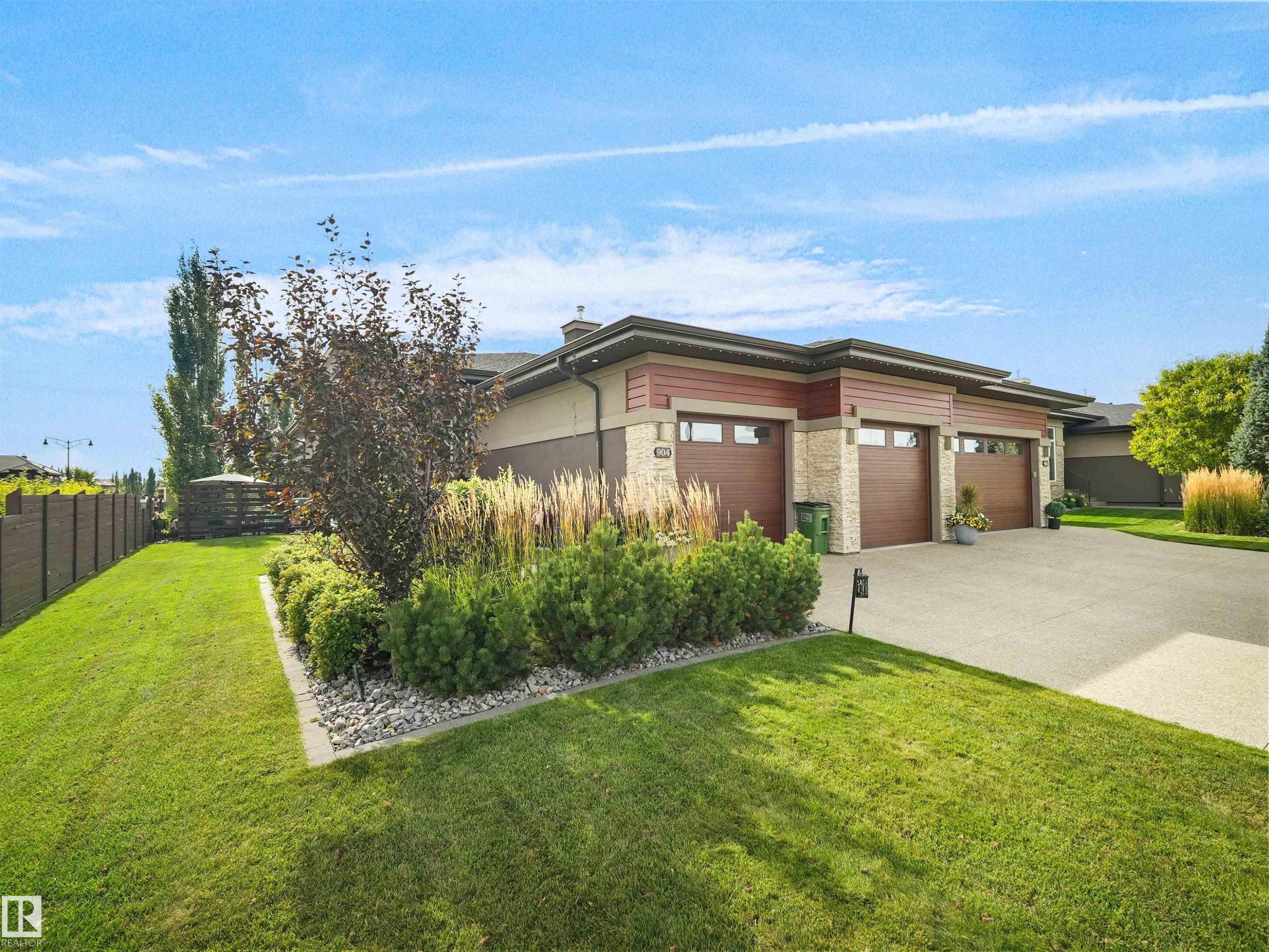 Contemporary exterior featuring stone accents, a multi-car garage with wood-finish doors, a concrete driveway, and landscaped garden beds - 904 Wood Place Nw, Edmonton, AB