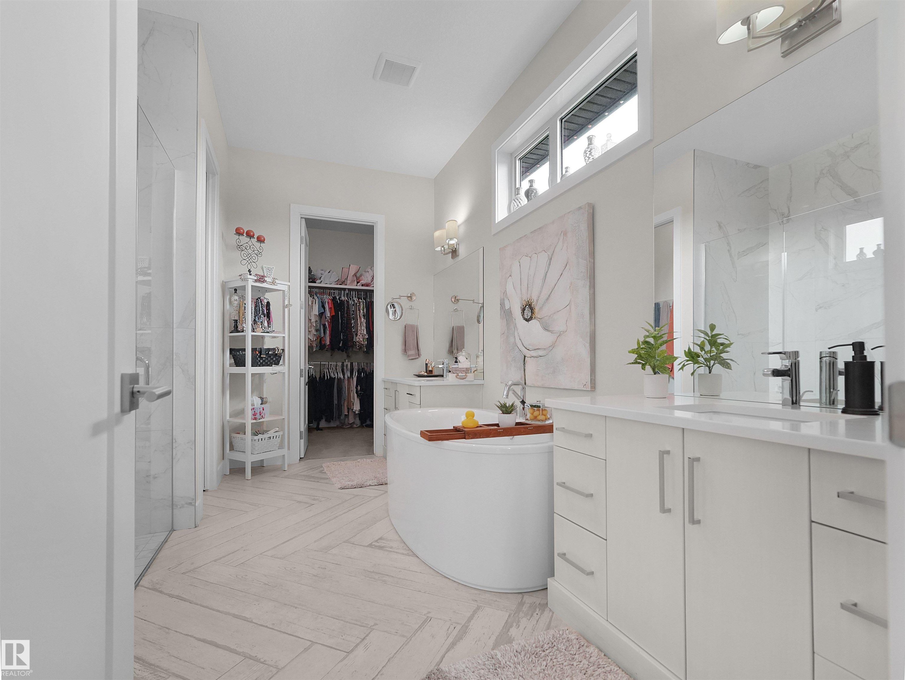 Freestanding soaking tub, dual vanity with undermount sinks, separate glass-enclosed shower, walk-in closet, and light-toned tile flooring in a herringbone pattern - 904 Wood Place Nw, Edmonton, AB