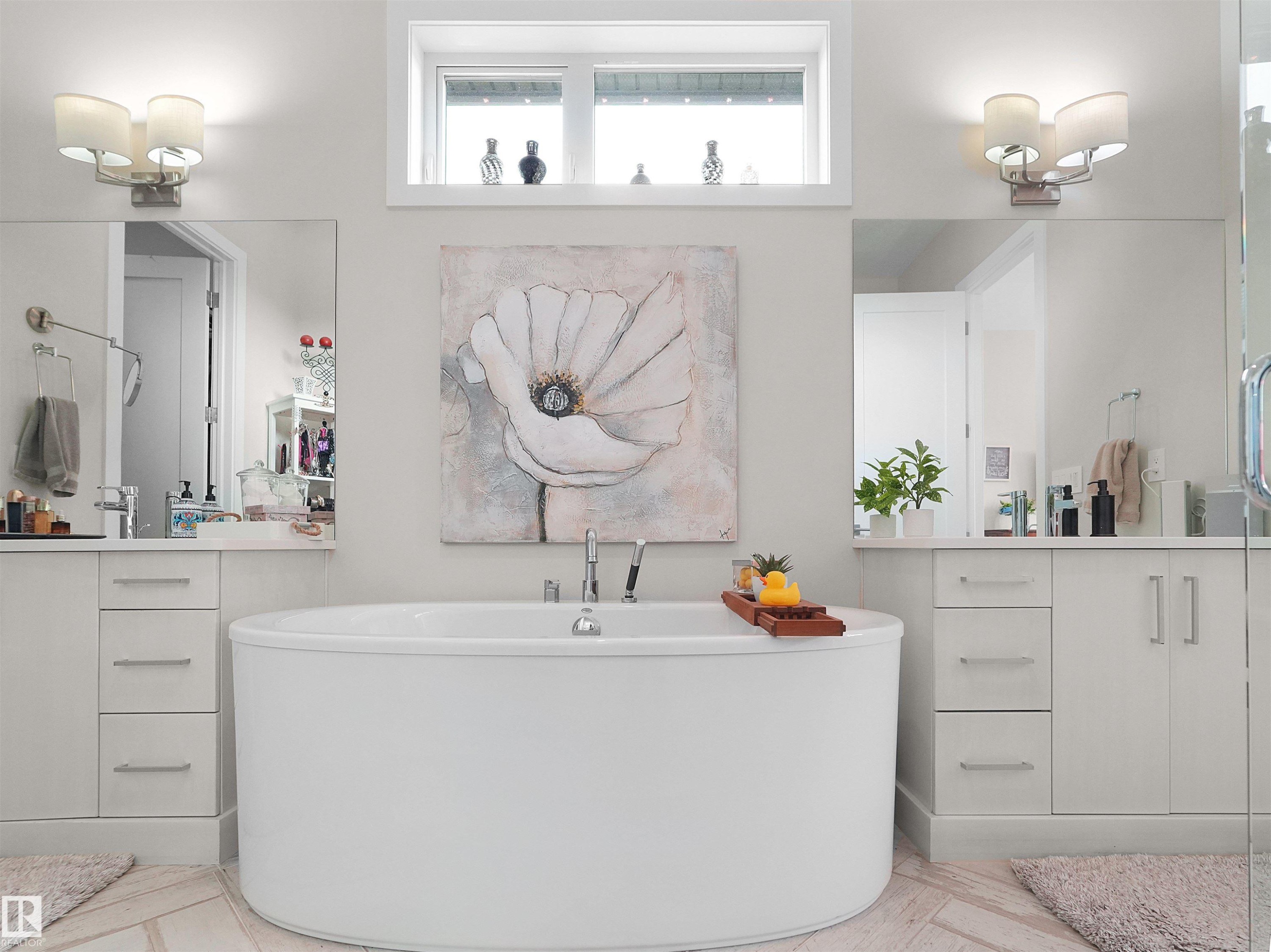 Freestanding oval soaking tub with floor-mounted tub filler, dual vanity sinks with white cabinetry, and a transom window - 904 Wood Place Nw, Edmonton, AB