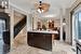 Kitchen featuring decorative columns, light stone counters, hanging light fixtures, dark brown cabinets, and crown molding