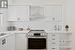 Kitchen with electric stove, wall chimney range hood, light countertops, and white cabinetry