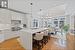 Kitchen featuring an island with sink, white cabinets, decorative light fixtures, custom exhaust hood, and a raised ceiling