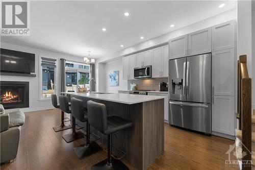 Gorgeous 2 toned kitchen with oversized island that accommodates 4 large stools and stainless steel appliances.  Hardwood floors throughout and patio doors leading to your backyard. - 637 Rathburn Lane, Ottawa, ON - Indoor Photo Showing Kitchen With Fireplace With Upgraded Kitchen