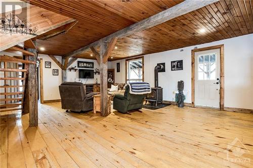 An open concept living area awaits on the main level with rustic wood beams, floors, and ceiling, and a wood stove. - 5258 Murphy Road, Calabogie, ON - Indoor Photo Showing Other Room