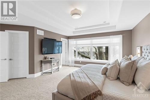 Large walk-in closet to the left of the television and oversized windows that showcase large deciduous tree as your backdrop in this tranquil primary room - 52 Moore Street, Ottawa, ON - Indoor Photo Showing Bedroom