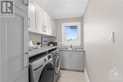 Laundry room is equipped with front-loading washer and dryer units, offering efficiency and convenience. Abundant storage space and a spacious counter provide ample room for organizing and folding - 52 Moore Street, Ottawa, ON - Indoor Photo Showing Laundry Room