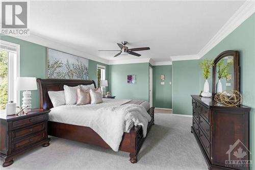A spacious primary bedroom on the second level with carpeted flooring, two bright windows, an en-suite bathroom, and a walk-in closet. Features beautiful ceiling moulding. - 2181 Des Grands Champs Way, Ottawa, ON - Indoor Photo Showing Bedroom