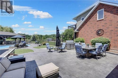 Covered cabana with a fully equipped bar, mounted TVs, and expansive seating area, overlooking the heated saltwater pool. - 551 Darby Road, Welland, ON - Indoor Photo Showing Other Room With In Ground Pool