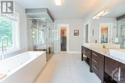 The primary bedroom's serene, spa-like ensuite features a heated porcelain tile floor with a wall-mounted thermostat, a vanity with a granite countertop and dual vessel sinks, and a wall-mounted m - 