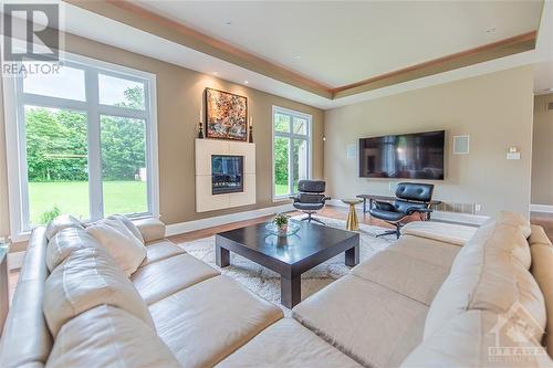 The family room is a delightful place to spend your evenings, featuring a 13' tray ceiling with recessed lighting, two windows that let in abundant natural light, and a contemporary wall-mounted g - 6163 Pebblewoods Drive, Ottawa, ON - Indoor Photo Showing Living Room With Fireplace
