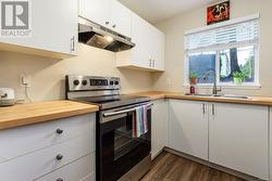 Kitchen with sink, butcher block countertops, dark wood-type flooring, stainless steel electric range oven, and white cabinets - 